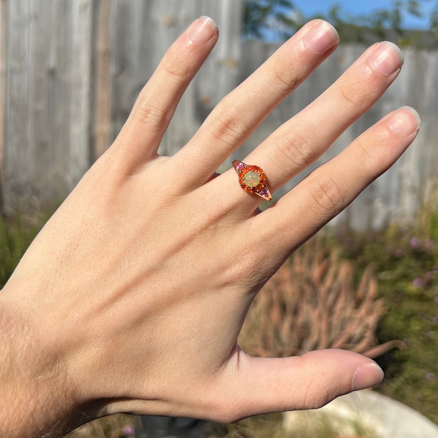 A yellow gold ring mounted with a round Ethiopian opal in a halo of faceted Mexican fire opals. Two pear shaped pink tourmalines accent the sides of the ring.