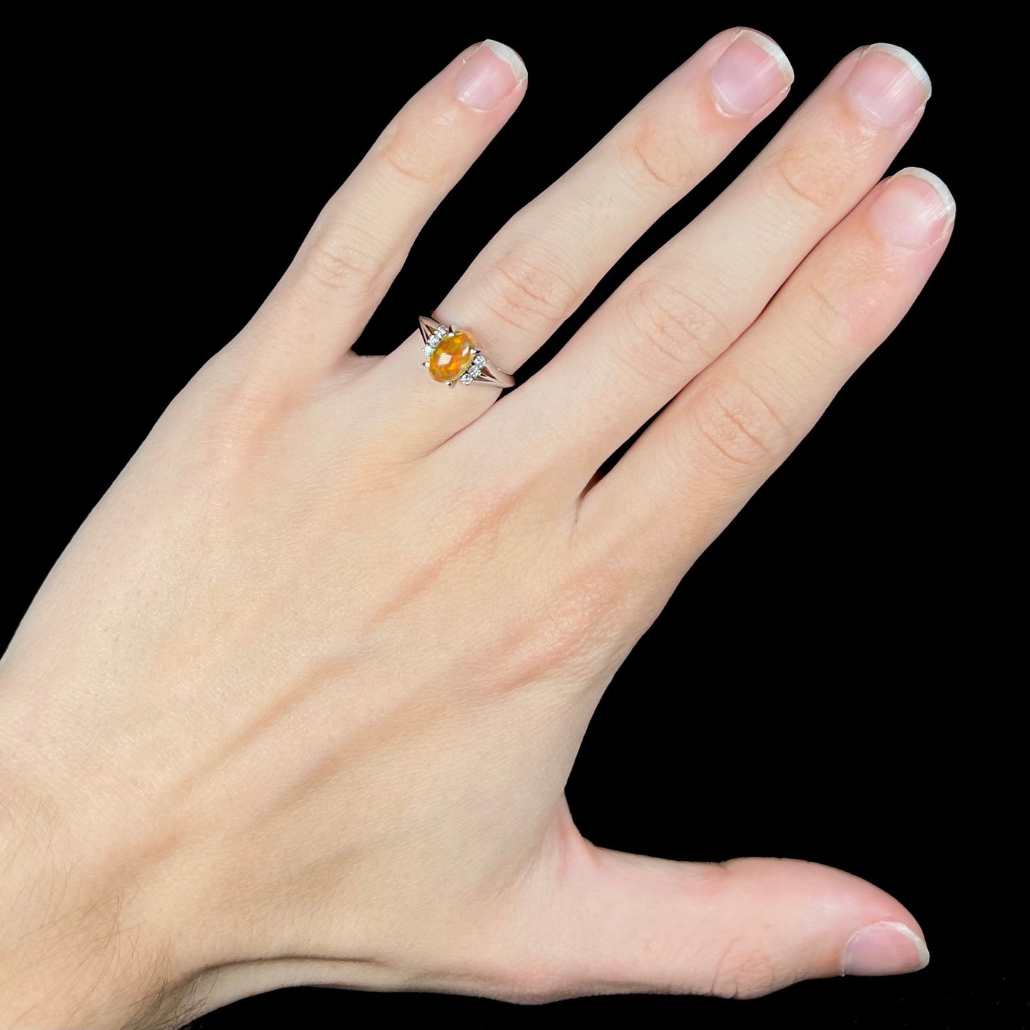 A platinum filigree and diamond-accented Mexican fire opal ring. The opal is orange with green fire.