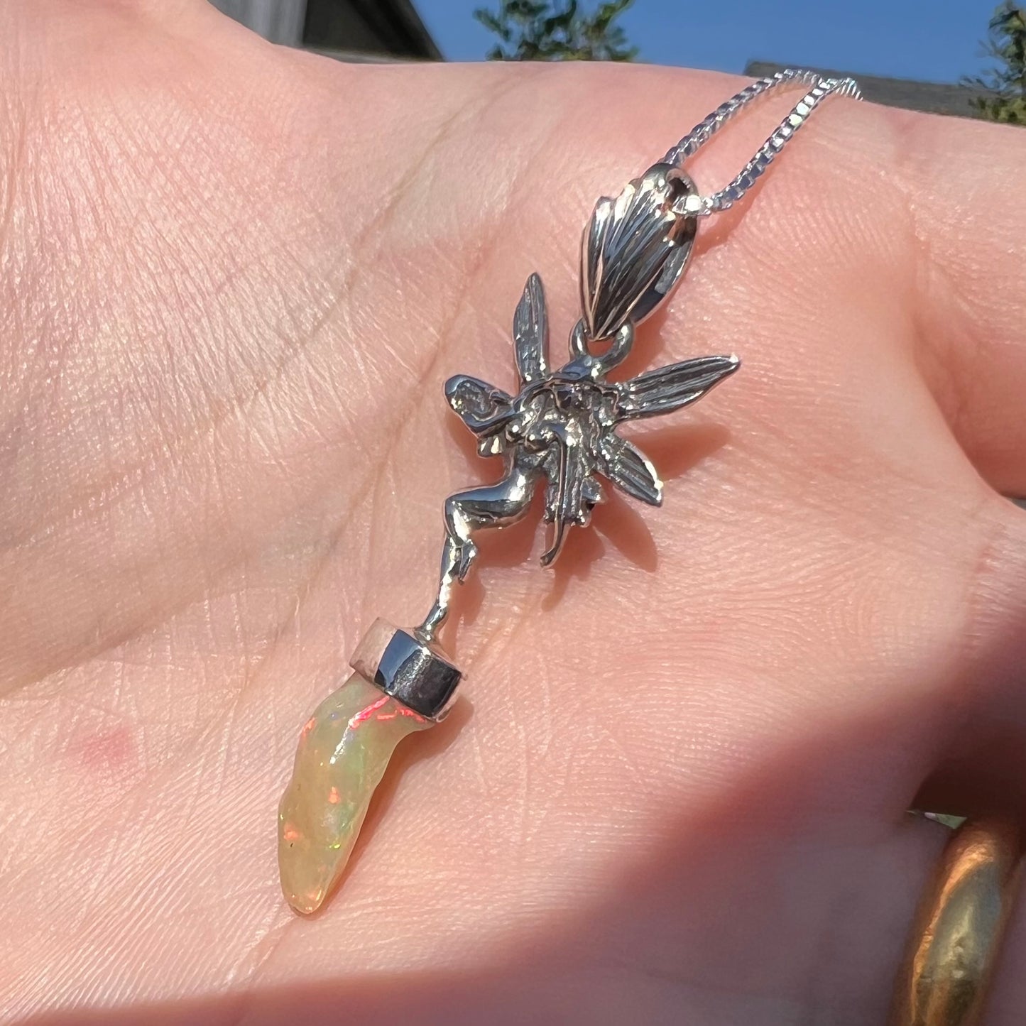 A sterling silver fairy necklace with an Ethiopian fire opal crystal, shown at an angle in a hand in sunlight.