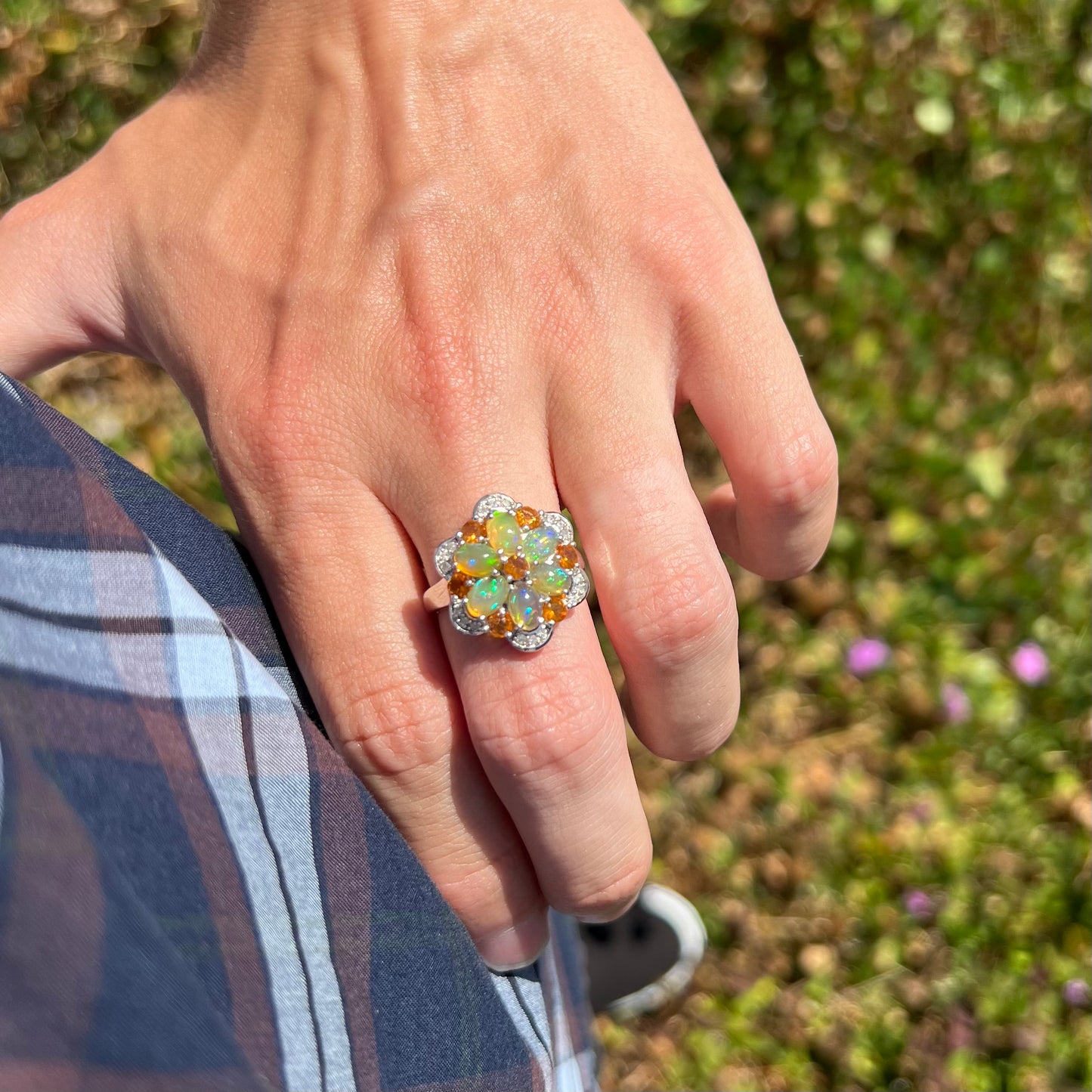 A person resting their hand on their hip while wearing a fire opal flower ring in natural daylight.