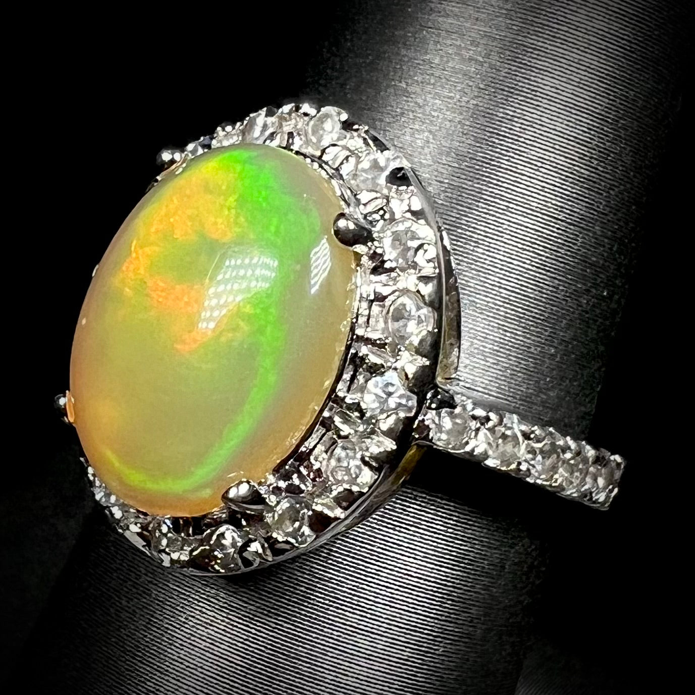 A sterling silver Ethiopian fire opal ring with a CZ halo shown at an angle against a black background.