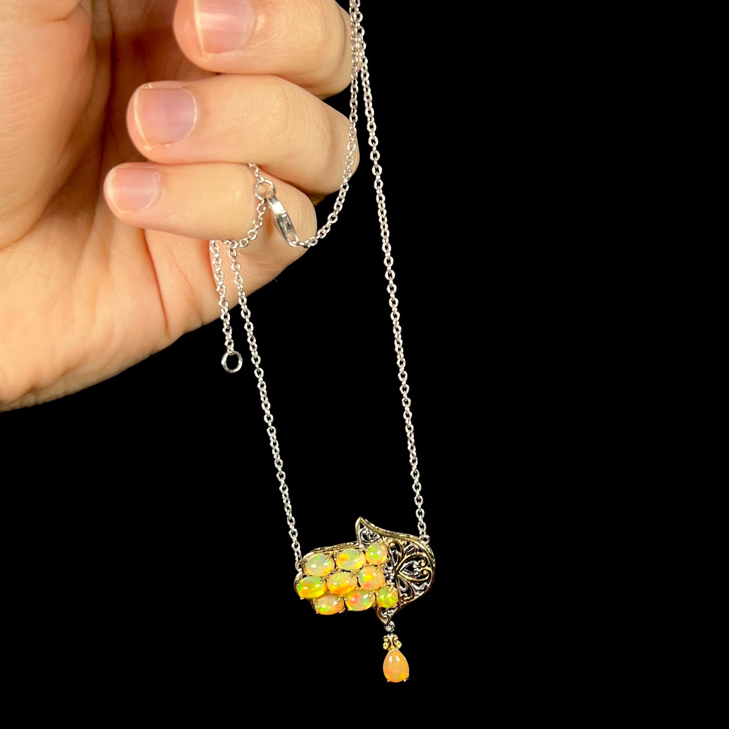 A fire opal hamsa necklace held from a hand by the chain.