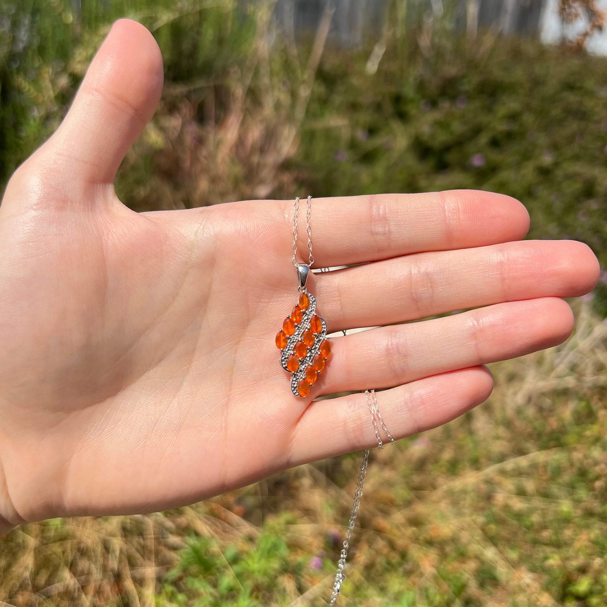 A fire opal pendant featuring a cluster of orange Mexican opals, held in a hand at a distance in sunlight.