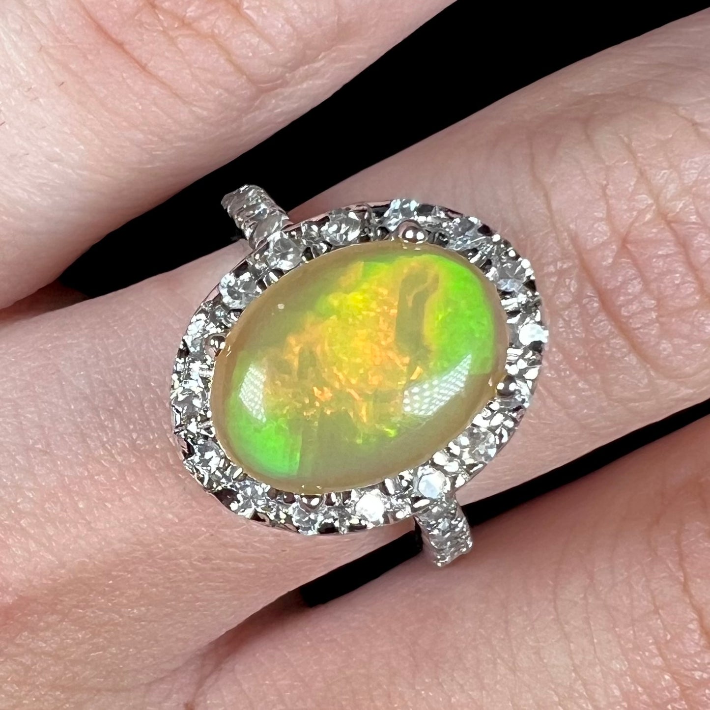 A sterling silver Ethiopian fire opal ring with a CZ halo shown close-up from the front on a hand.