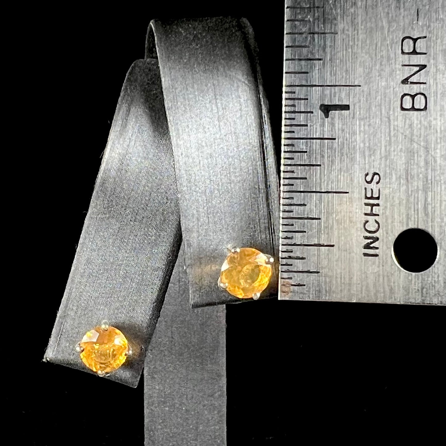 A pair of Mexican fire opal stud earrings in sterling silver held next to a ruler for scale.