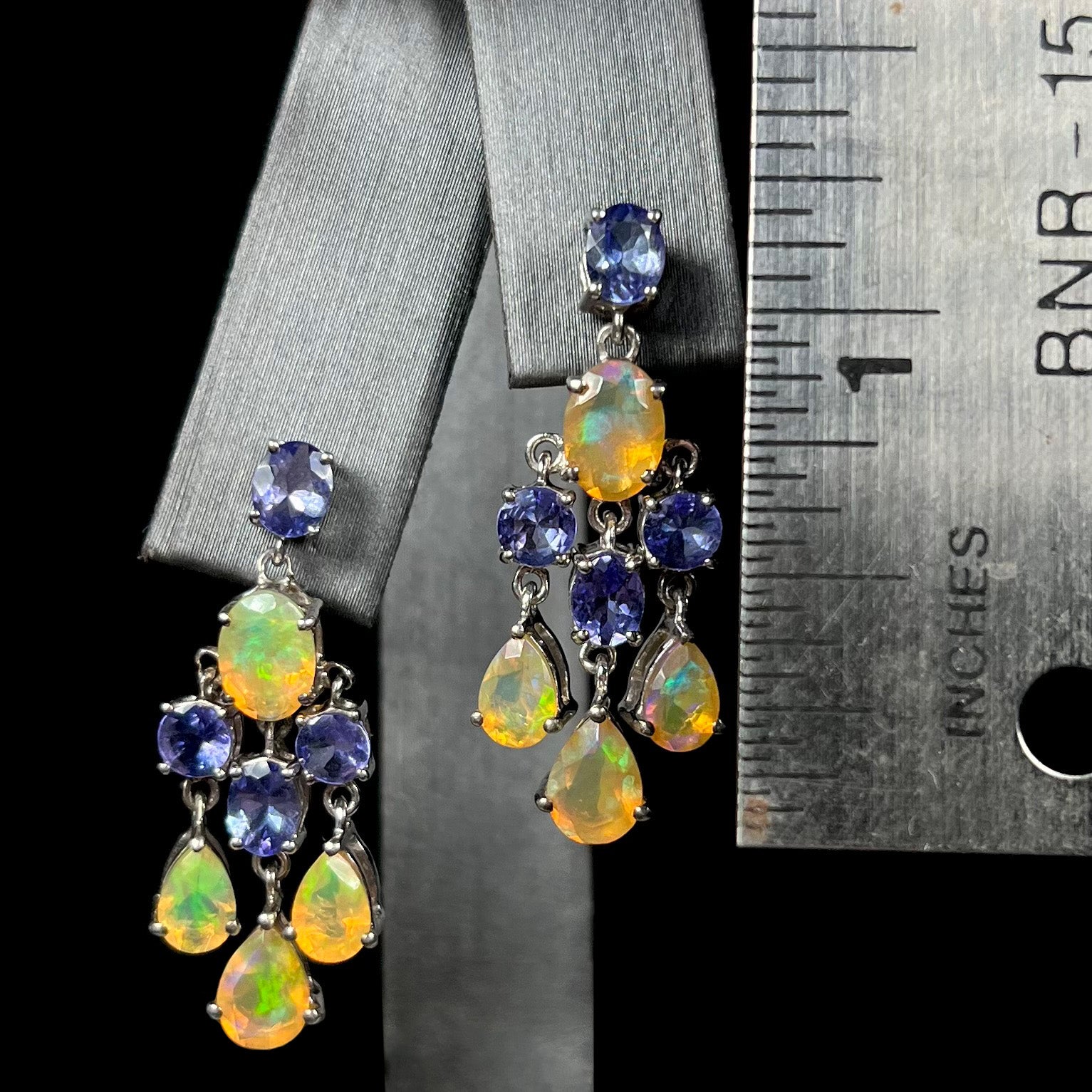 A pair of dangling sterling silver opal and tanzanite chandelier earrings next to a ruler, measuring 1.25 inches.