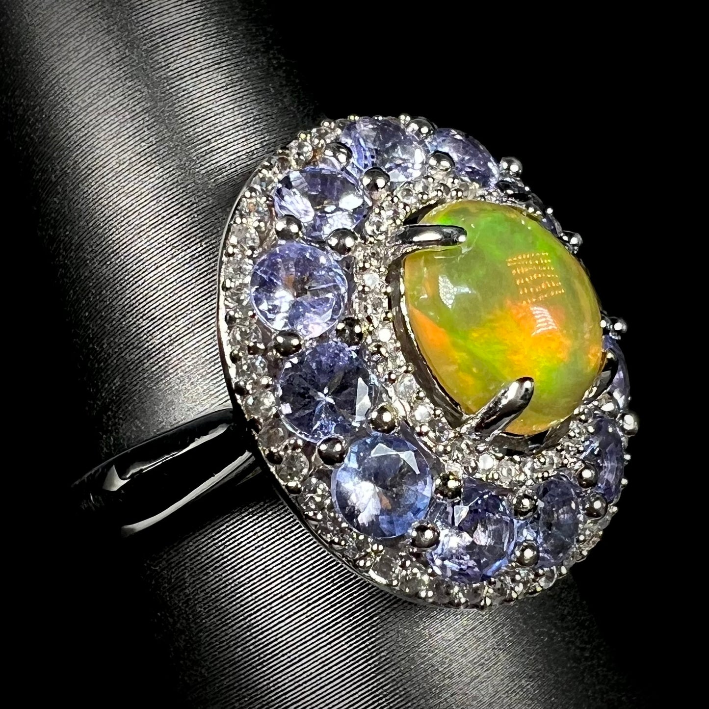Angled view of ring with Ethiopian fire opal set in halo of white zircons and tanzanite.