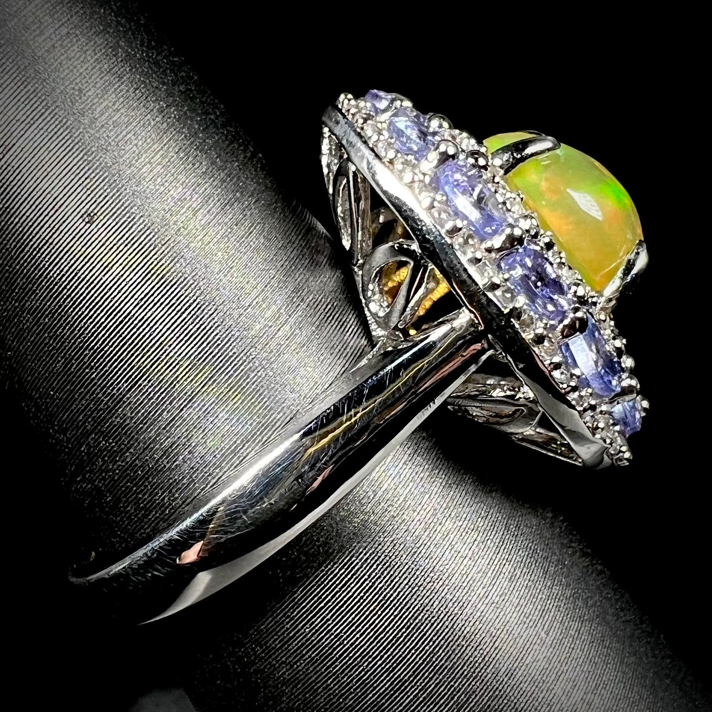Side view of silver Ethiopian fire opal ring with tanzanite halo. Ring's shank in focus.
