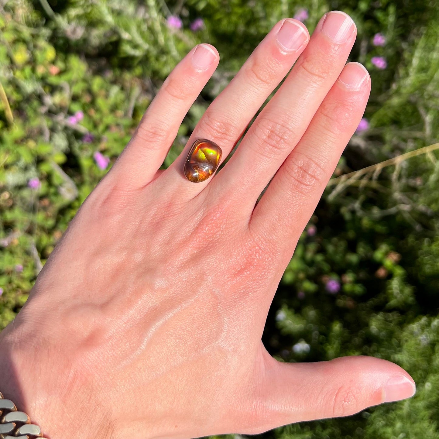 A loose fire agate cabochon. The stne shows green and orange iridescence on a brown body tone.