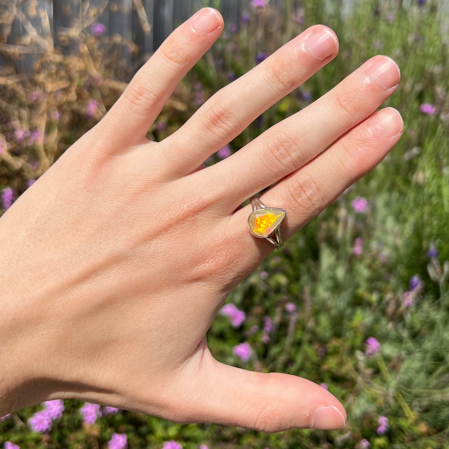 A unisex sterling silver ring set with a faceted pear shaped Ethiopian fire opal. The opal plays orange, red, and green colors.