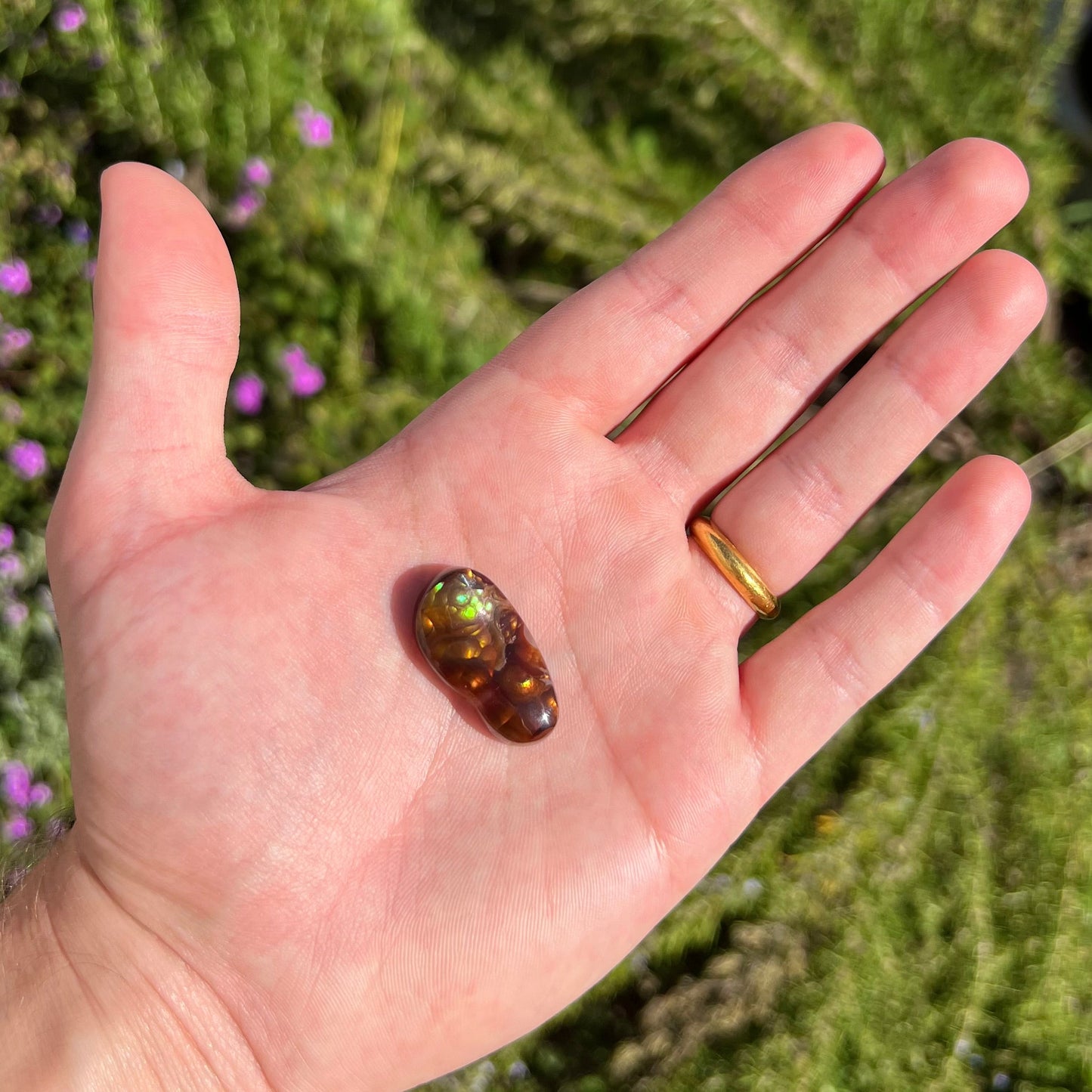 A loose fire agate cabochon. The stone has iridescent green, yellow, and blue colors.