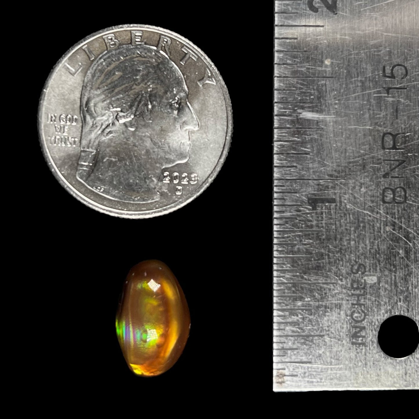 A loose, oval cabochon cut fire agate stone that shines red, yellow, green, blue, and purple.