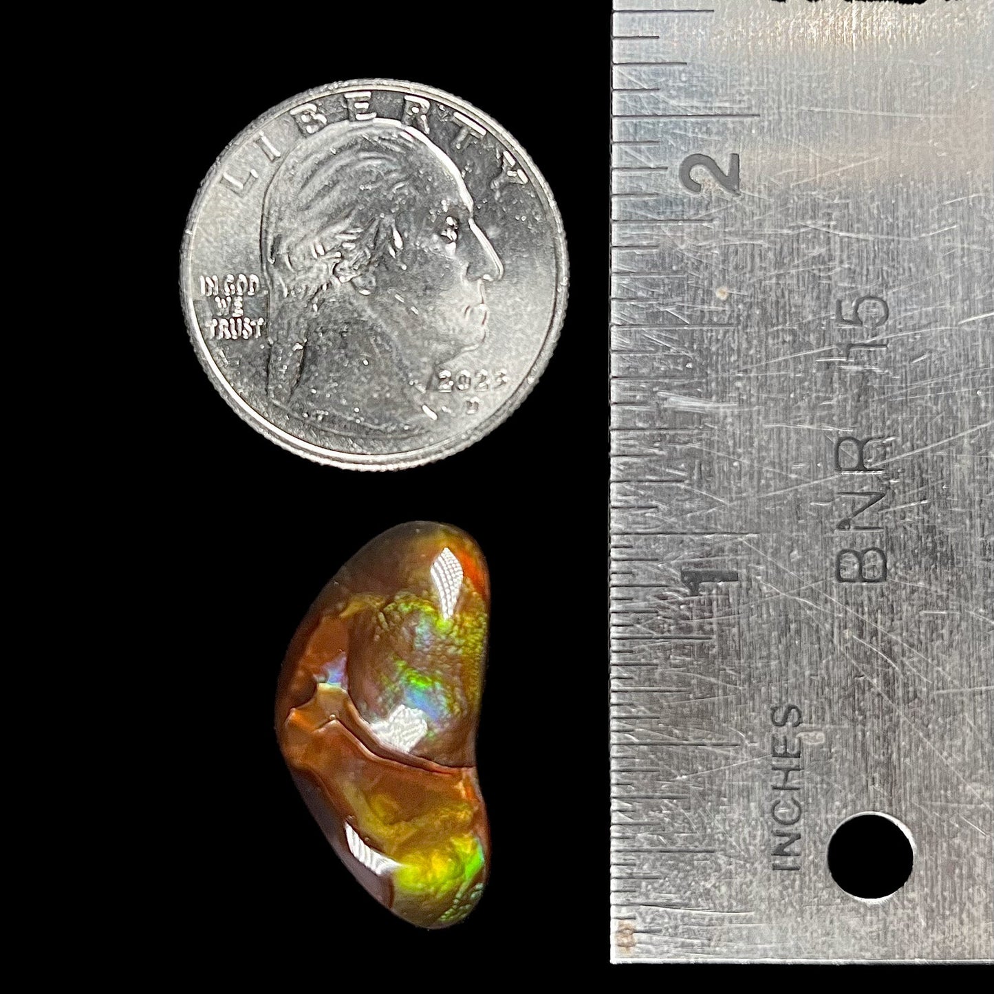A loose, boomerang shaped fire agate cabochon. The stone displays greens, purples, blues, and reds.