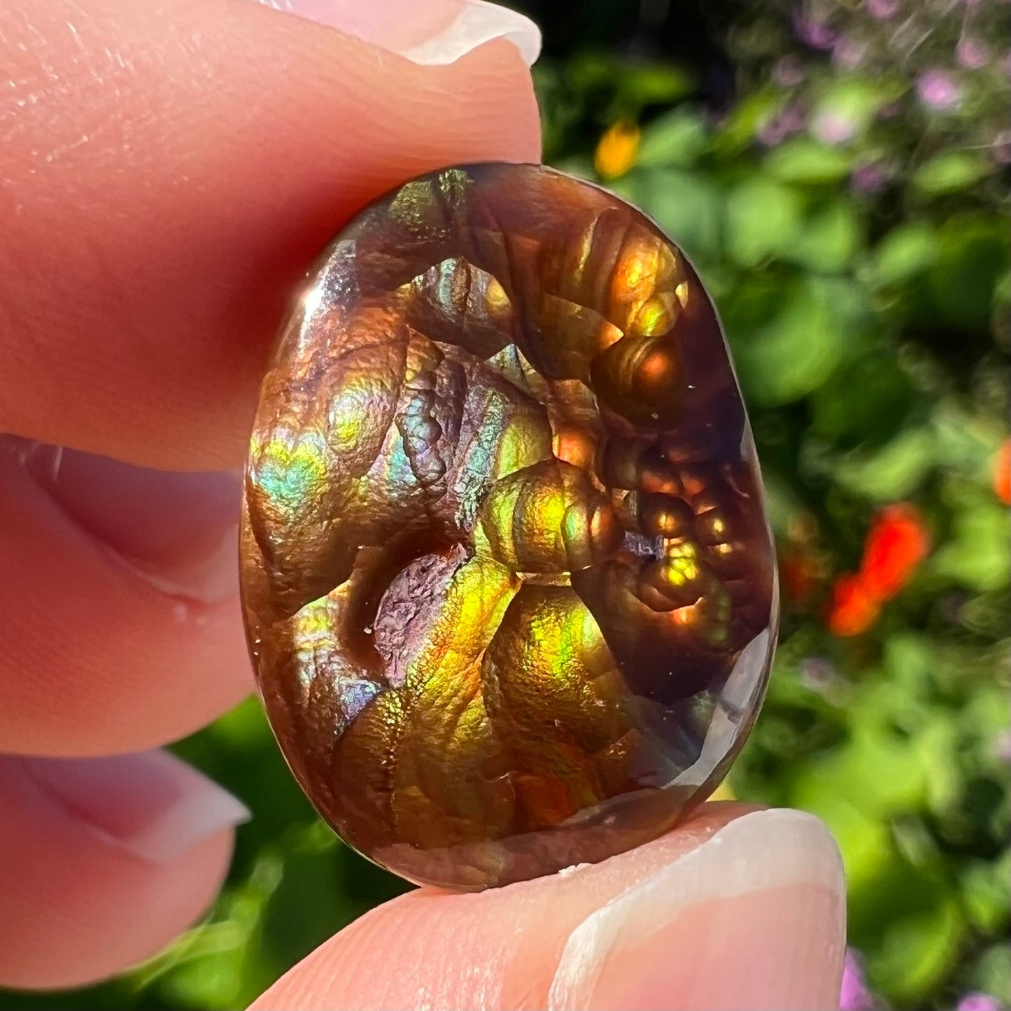 An oval cabochon cut Mexican fire agate stone. The stone's predominant colors are green, yellow, orange, and blue.