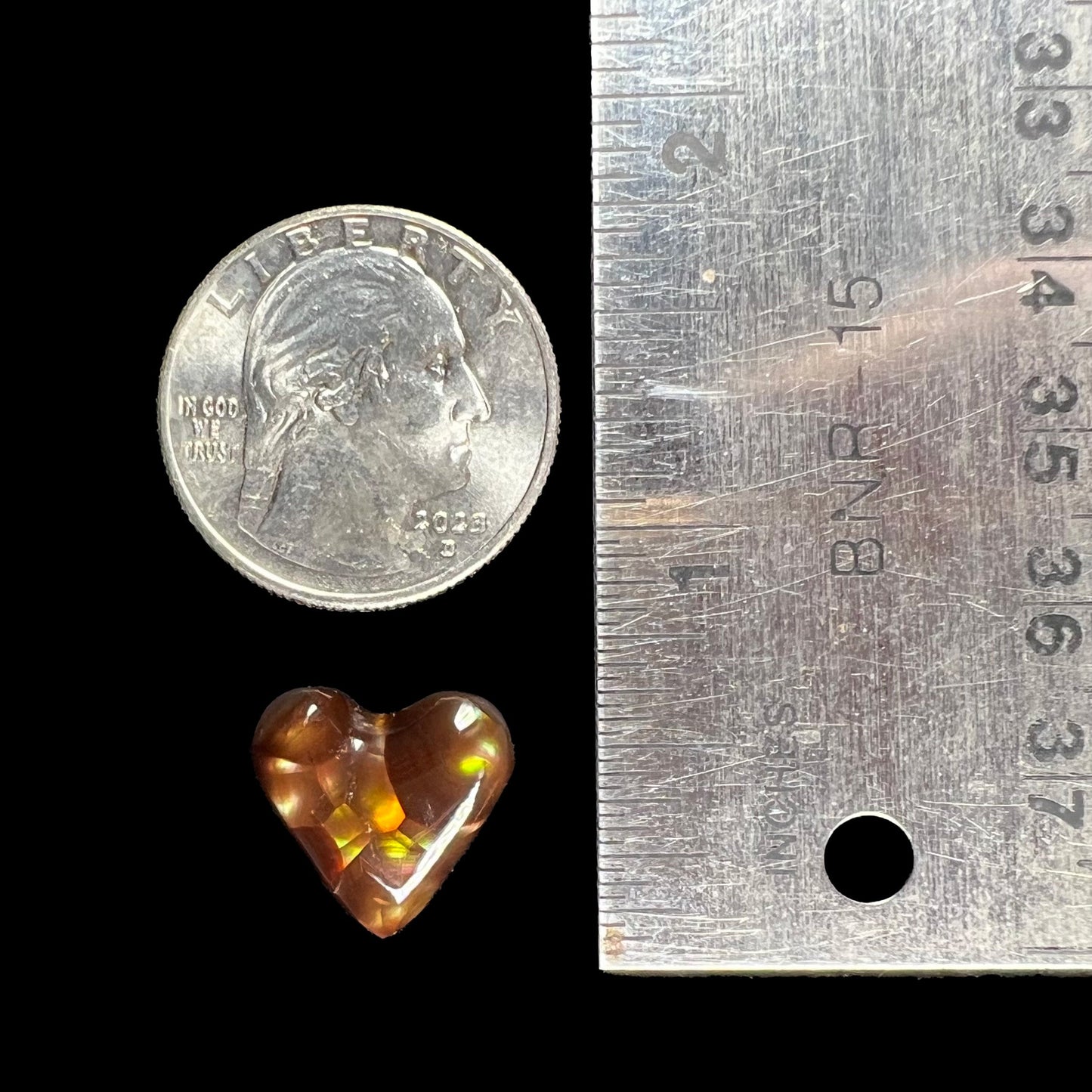 A cabochon cut heart shaped Mexican fire agate stone. The stone is orange, yellow, pink, green, and purple.