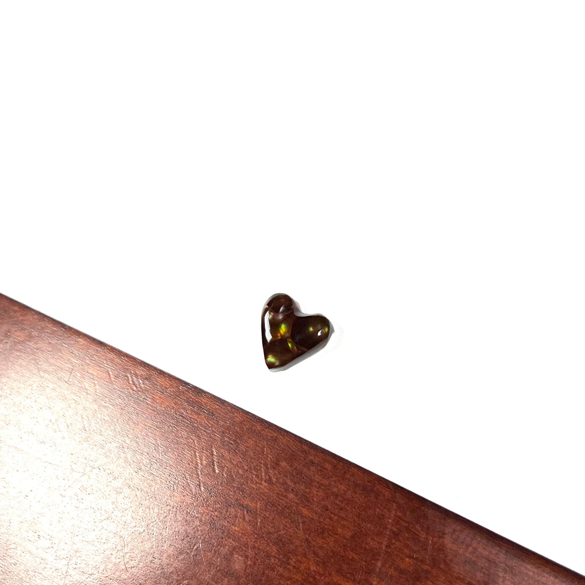 A cabochon cut heart shaped Mexican fire agate stone.  The stone is orange, yellow, pink, green, and purple.