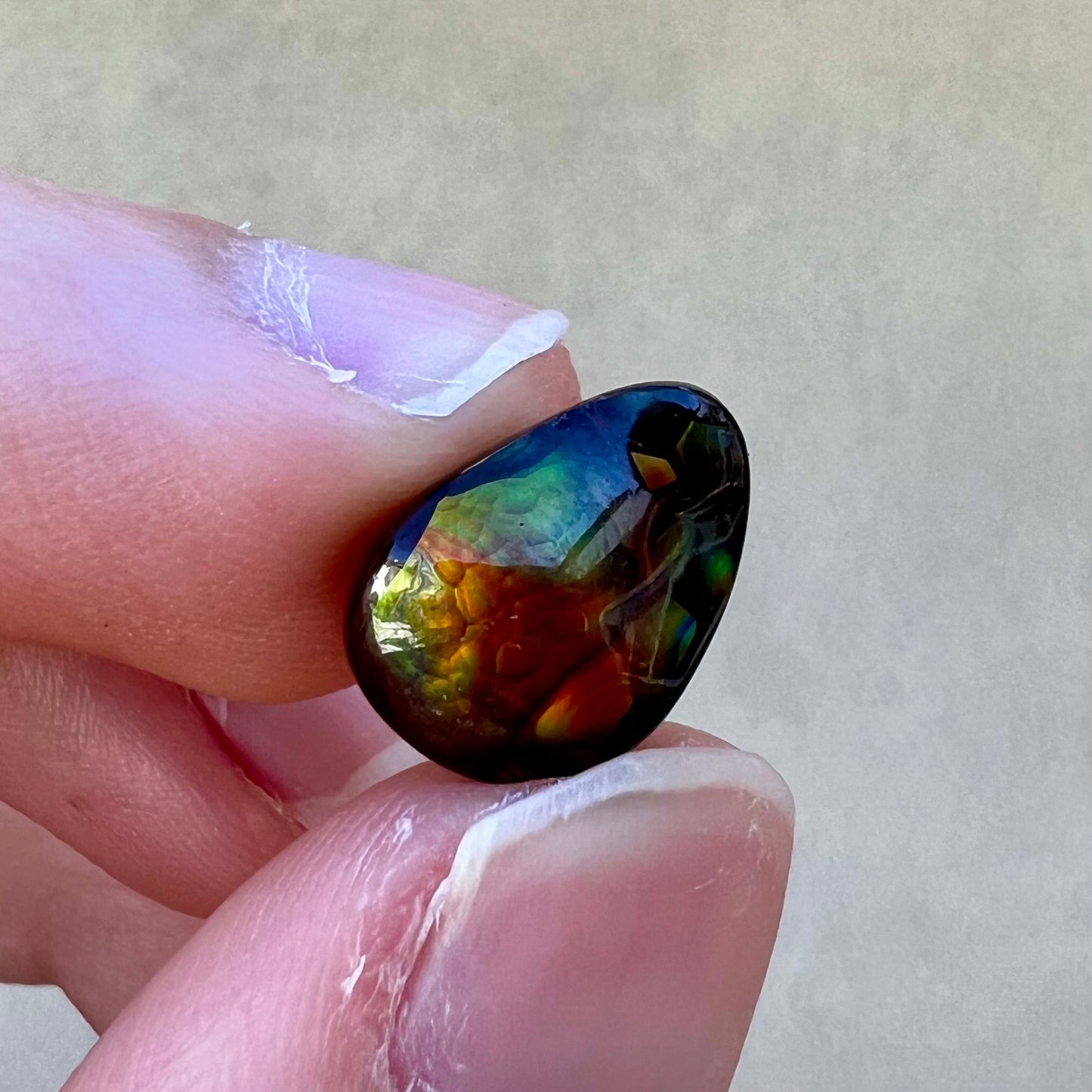 A loose, pear shaped fire agate stone from Northern Mexico. The stone is red and green with blue banding.