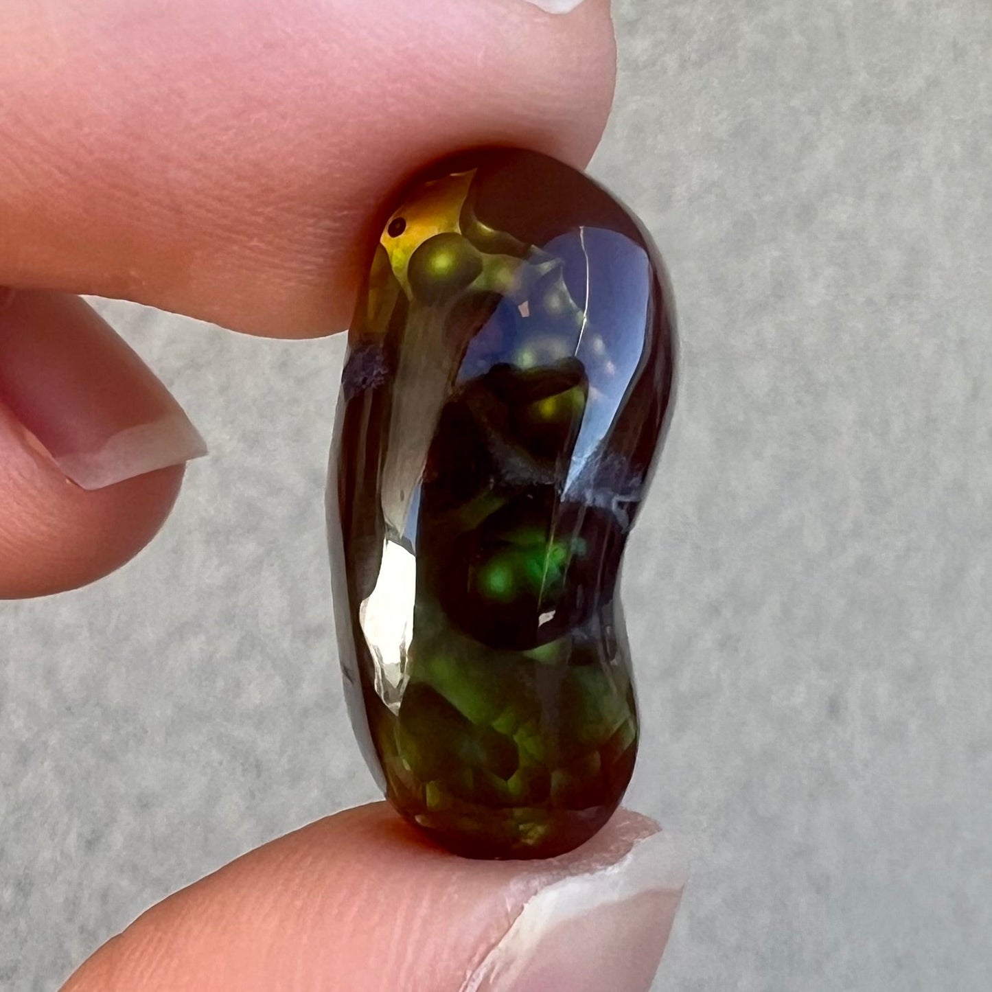 A loose, cabochon cut fire agate gemstone. The stone resembles a foot with a green heel and yellow toes.
