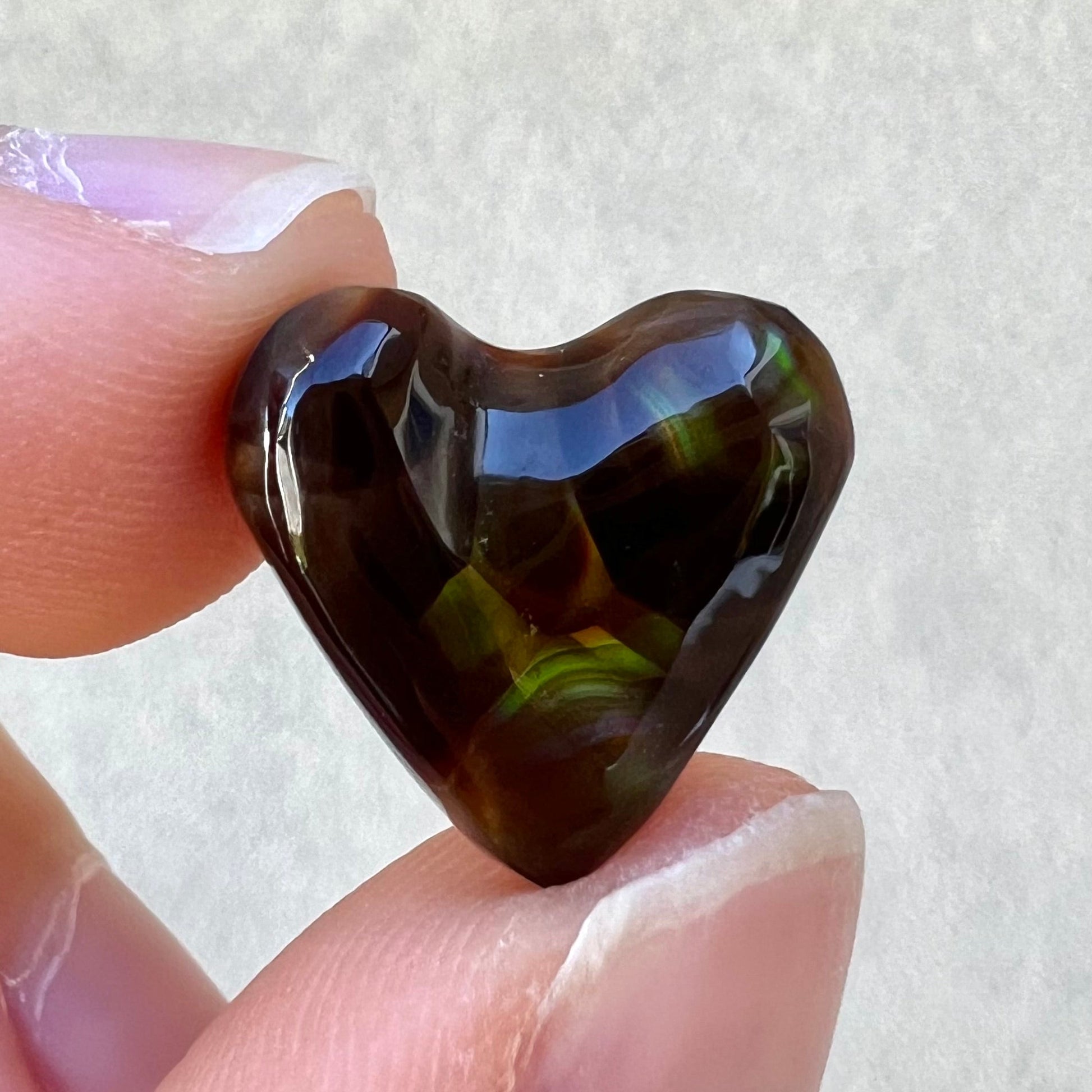 A cabochon cut heart shaped Mexican fire agate stone.  The stone is orange, yellow, pink, green, and purple.