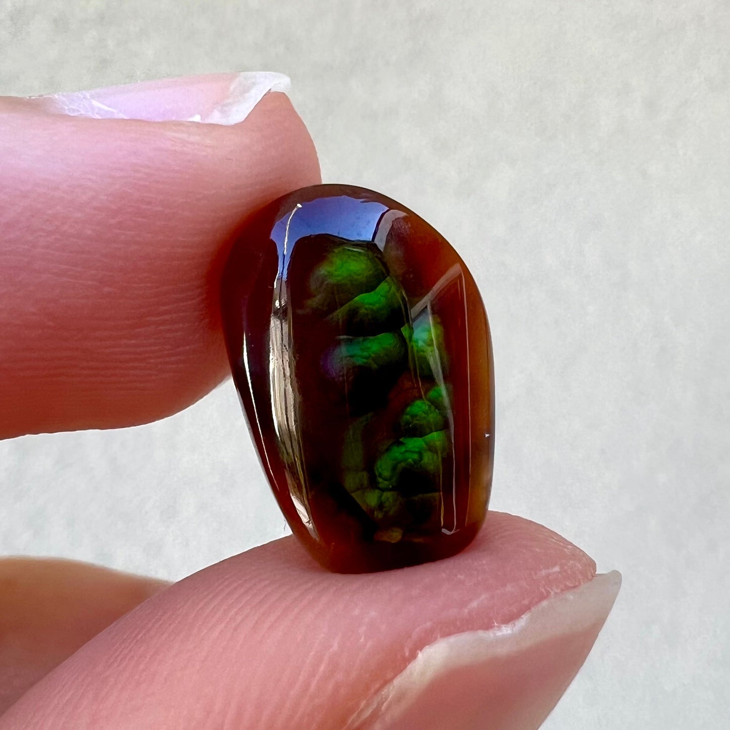 A loose, freeform cabochon cut fire agate gemstone. The stone is green with blue overtones.