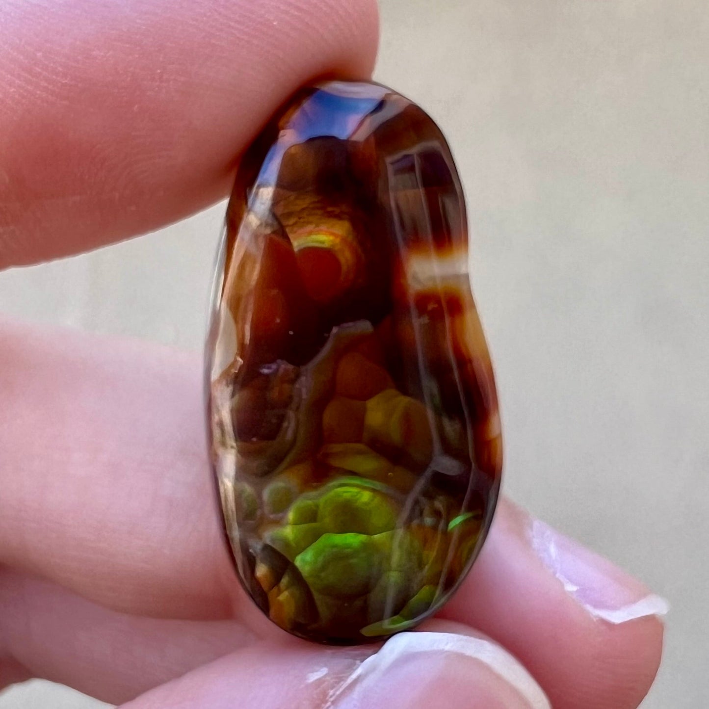 A loose fire agate cabochon. The stone has iridescent green, yellow, and blue colors.