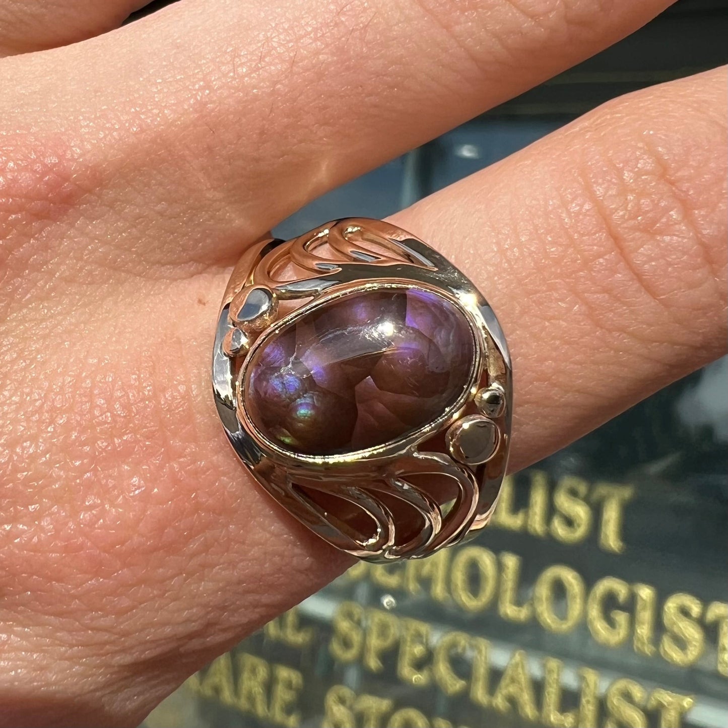 An oval cabochon cut fire agate with purple and blue colors set in a yellow gold men's ring.