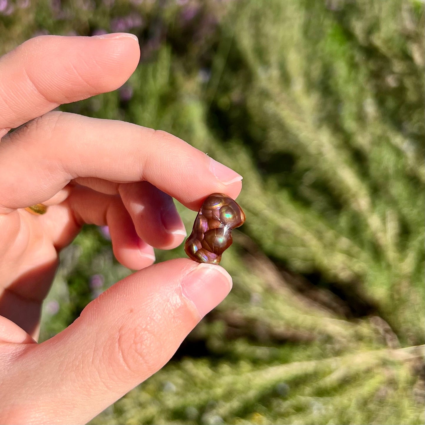 A polished, freeform shaped fire agate stone. The stone is purple, green, and blue with red and yellow banding.