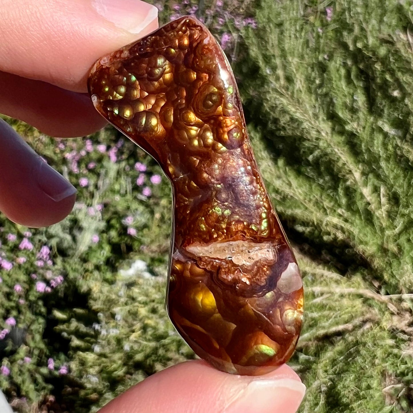 A loose, freeform cabochon cut fire agate gemstone. The stone exhibits a bubbly pattern.