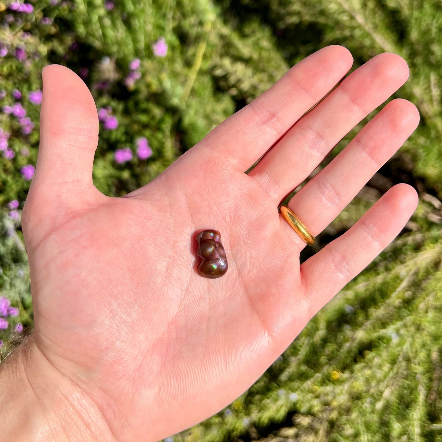 A polished, freeform shaped fire agate stone. The stone is purple, green, and blue with red and yellow banding.