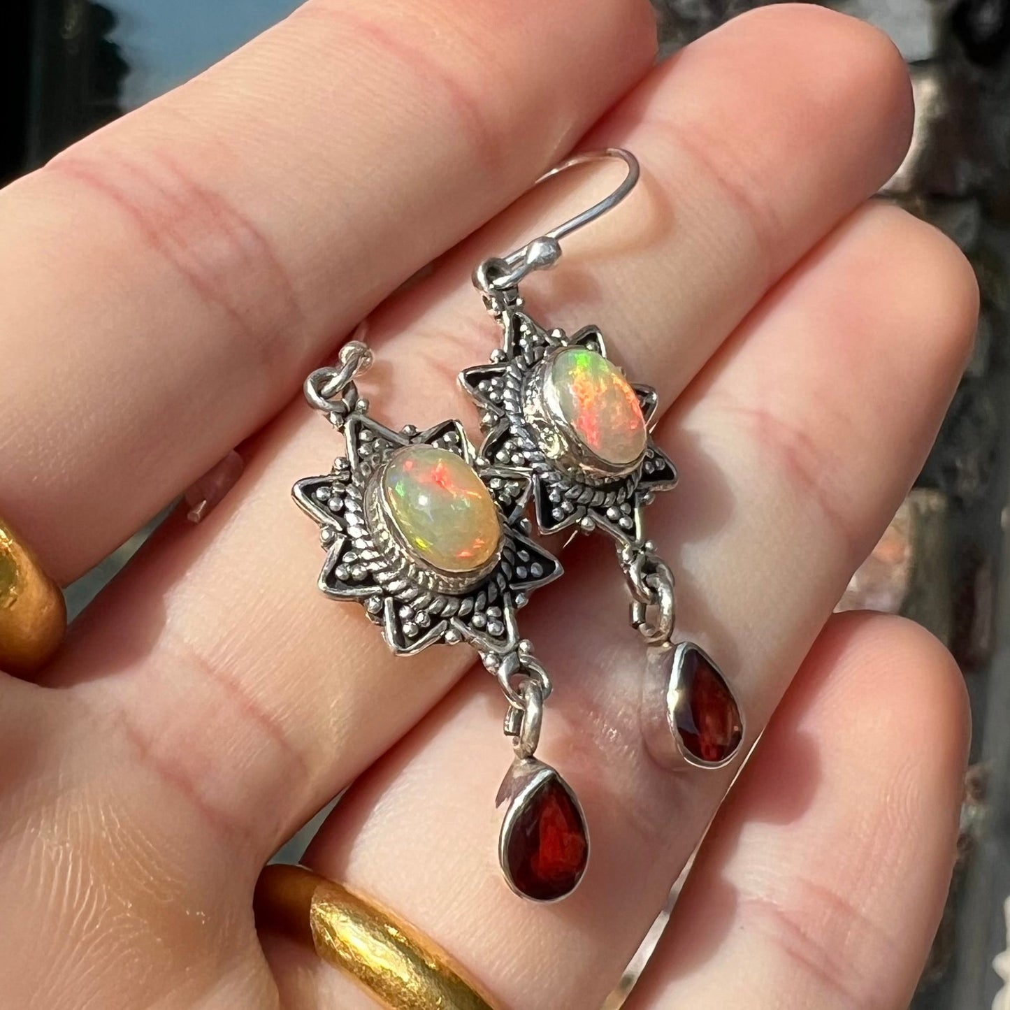 A pair of sterling silver star design dangle earrings set with Ethiopian fire opals and pear shaped red garnet accents.