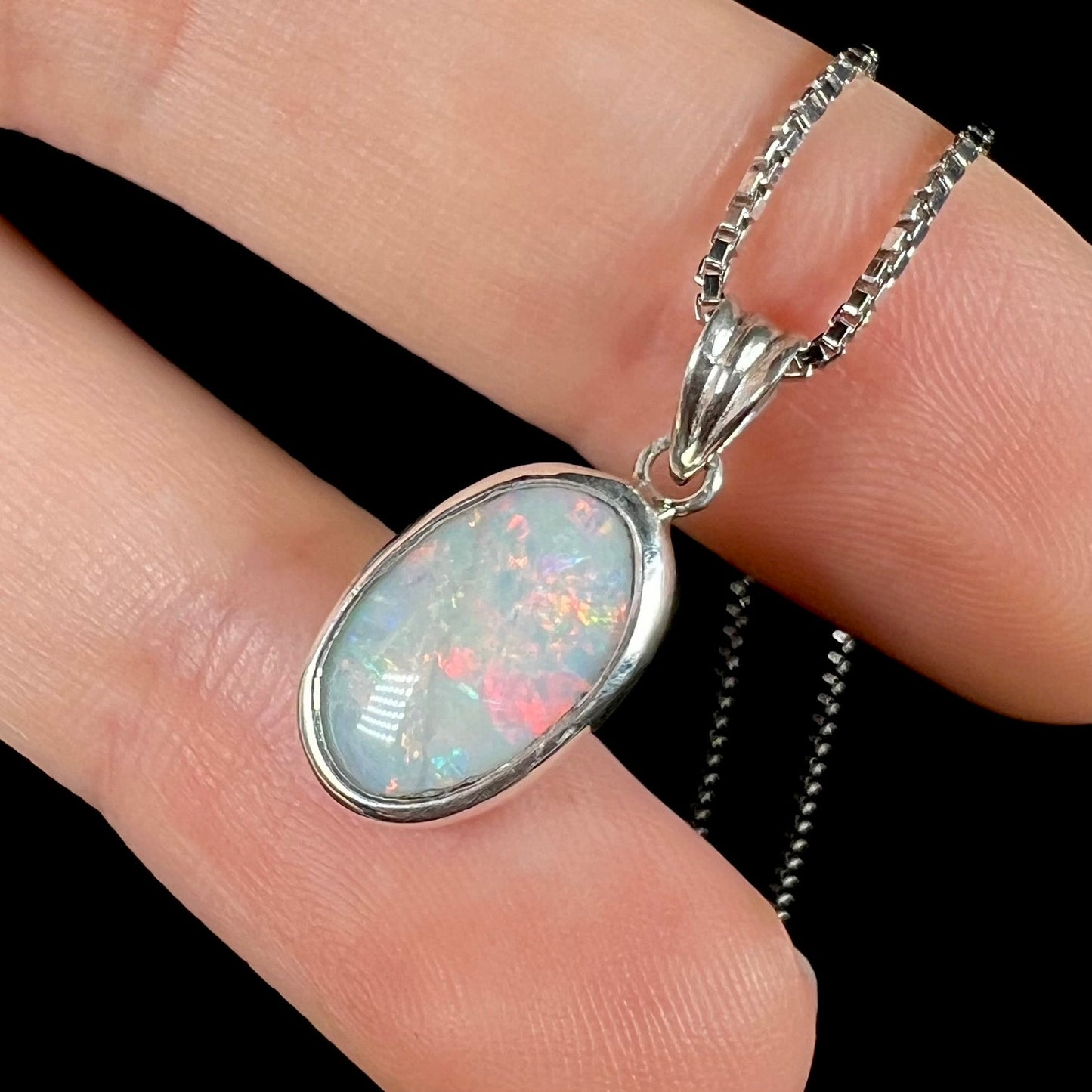 A ladies' sterling silver necklace bezel set with a natural white crystal opal. The opal has red and blue fire.