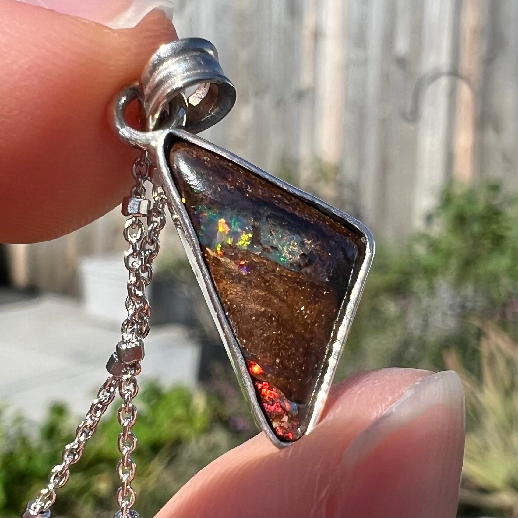 A sterling silver necklace bezel set with a triangle shaped boulder opal.  The opal has red and blue flashes.