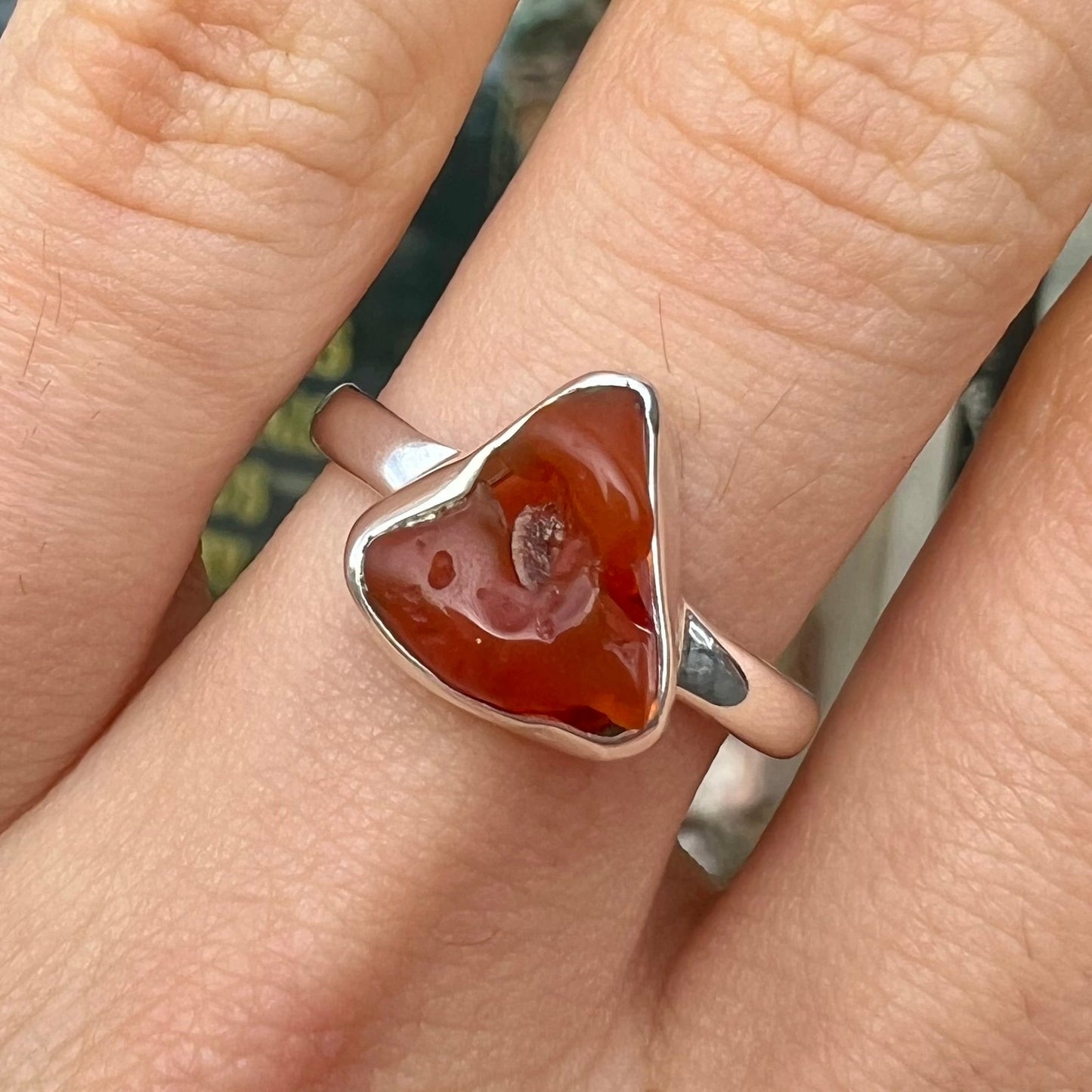 A polished fire opal crystal bezel set into a sterling silver ring. The opal is an orange color.