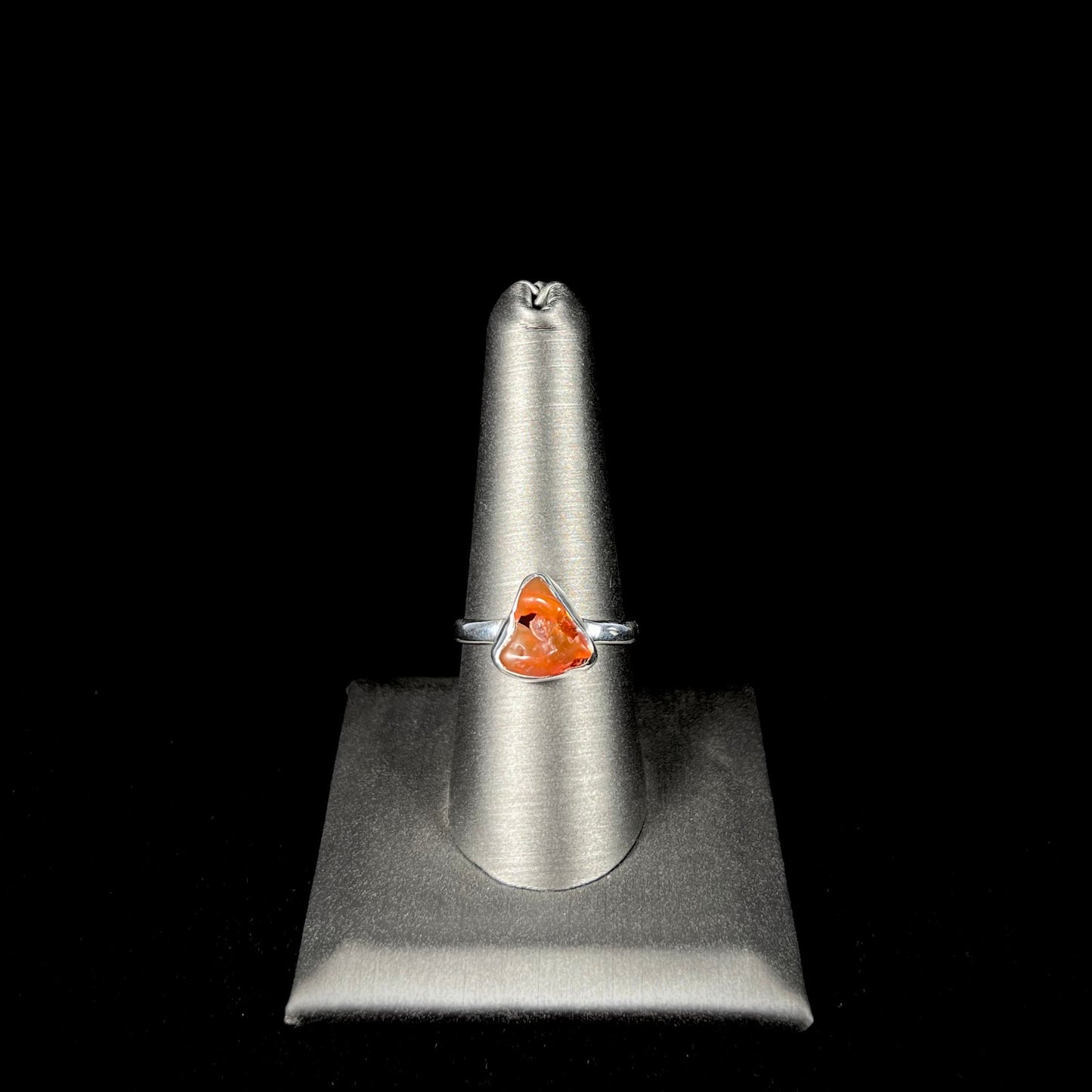 A polished fire opal crystal bezel set into a sterling silver ring. The opal is an orange color.