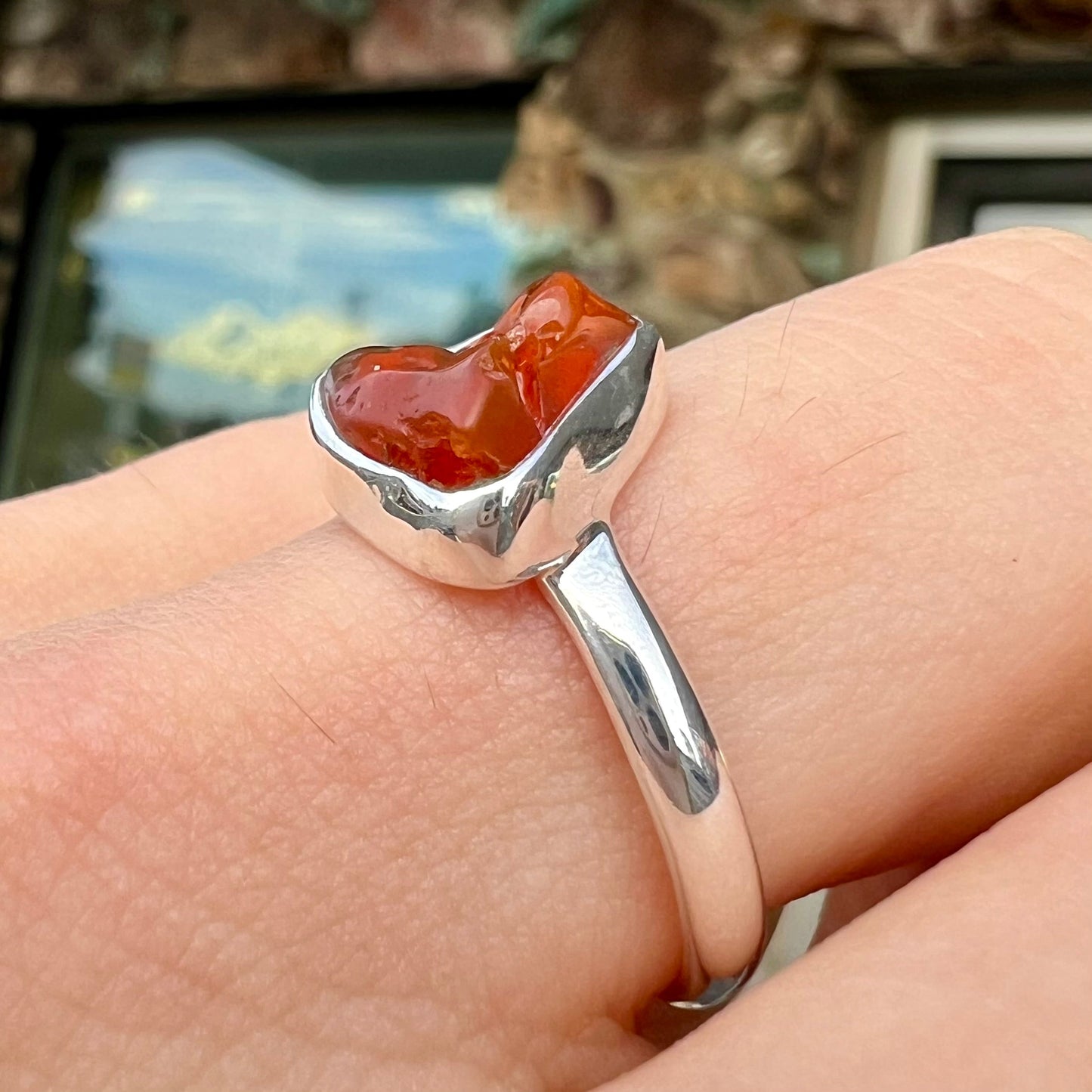 A polished fire opal crystal bezel set into a sterling silver ring. The opal is an orange color.