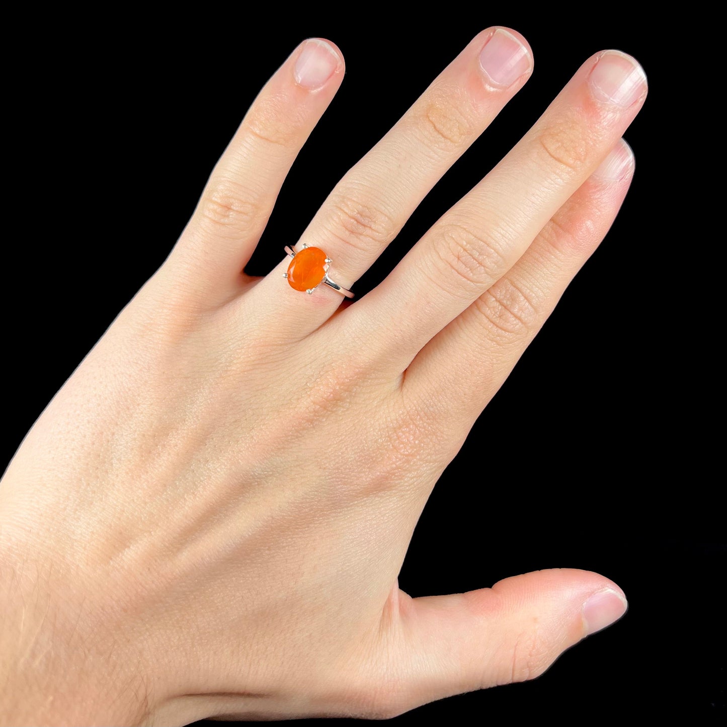A silver solitaire ring set with a natural, faceted oval cut Mexican fire opal. The stone is a bright orange color.