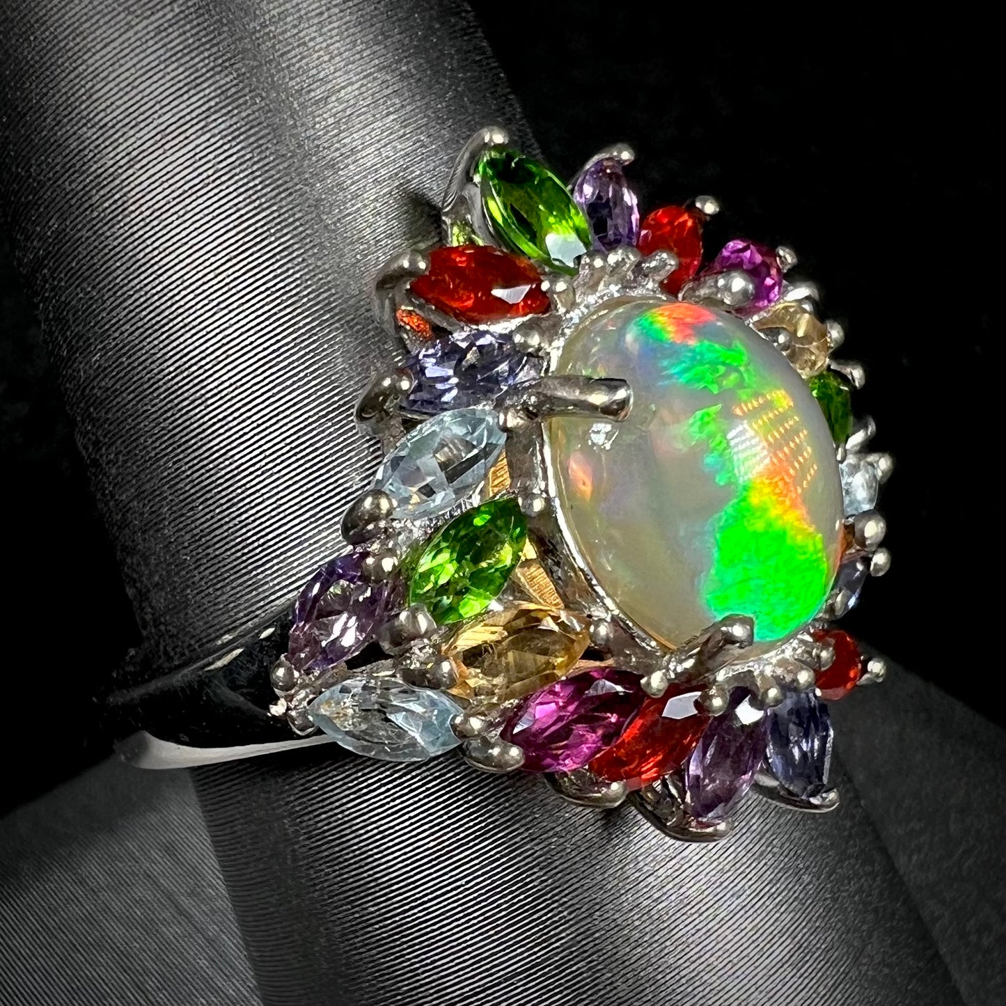 A flamboyant multi-gemstone opal ring with green color play, shown from an angle.