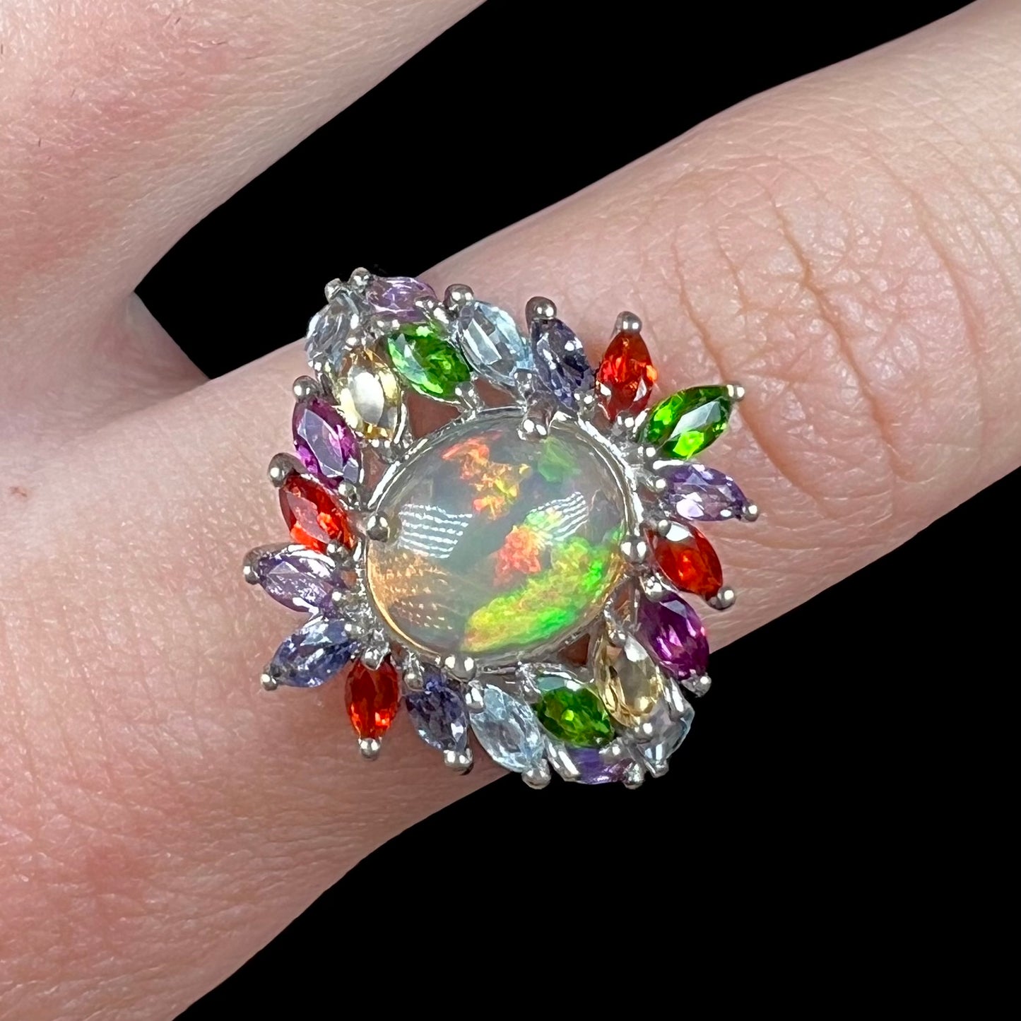 Close-up of a flamboyant opal multi-stone ring, worn on a finger and shown from the front.