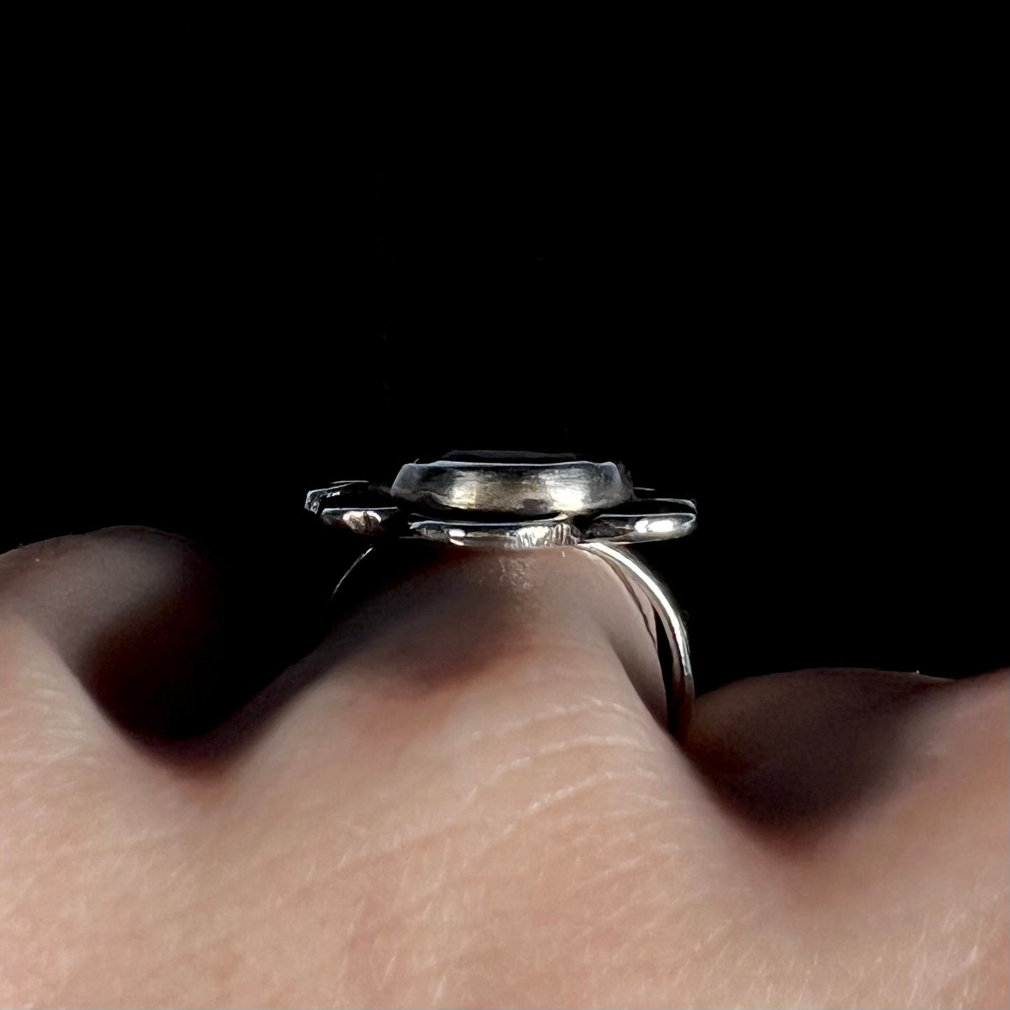 Side gallery view of fire agate ring worn on hand, black background.