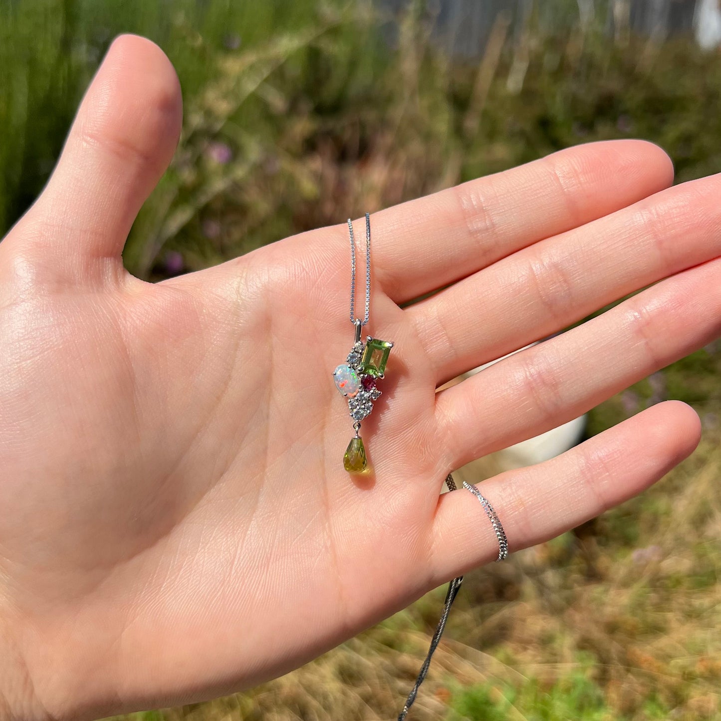 A gemstone cluster necklace held in a hand in the sunlight.