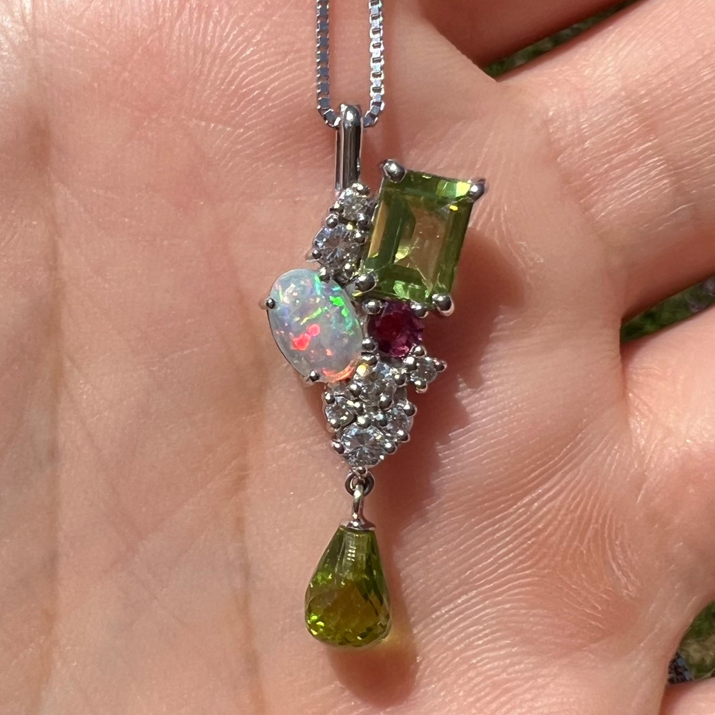 Close-up front view of a gemstone cluster pendant held in a hand in natural light.