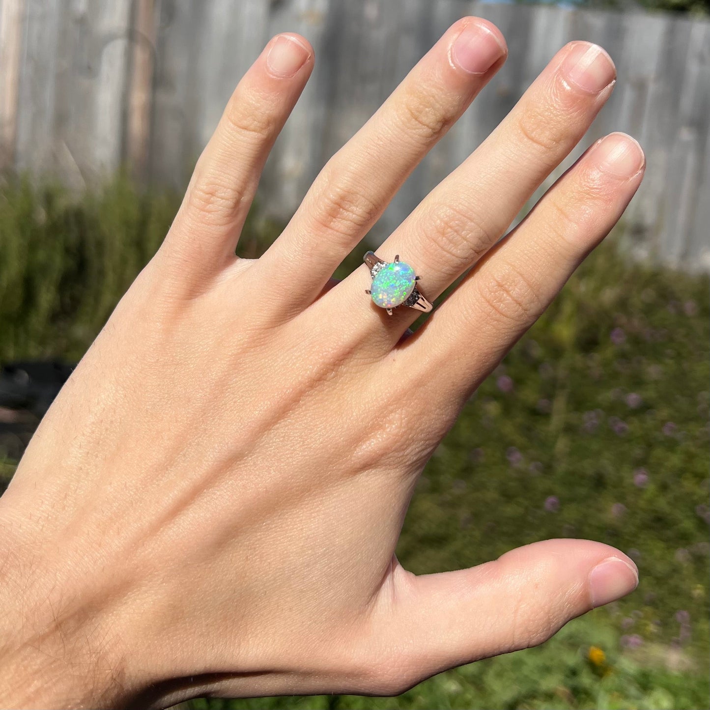 A platinum filigree opal engagement ring set with diamond accents. The opal has green-blue colors.