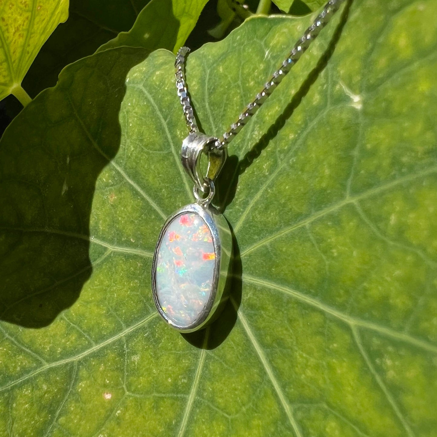 A ladies' sterling silver necklace bezel set with a natural white crystal opal. The opal has red and blue fire.