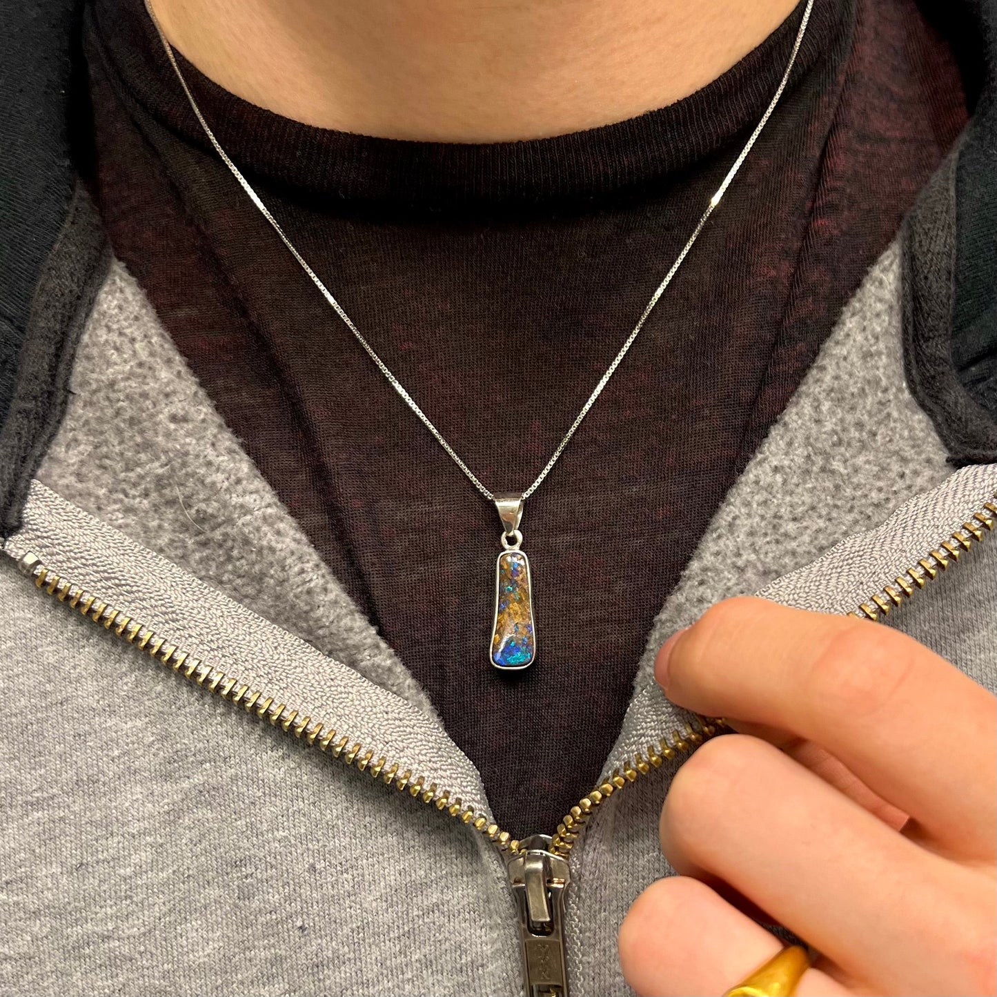 A sterling silver necklace bezel set with a natural Australian boulder opal stone. The stone shines colors of blue, green, and purple.
