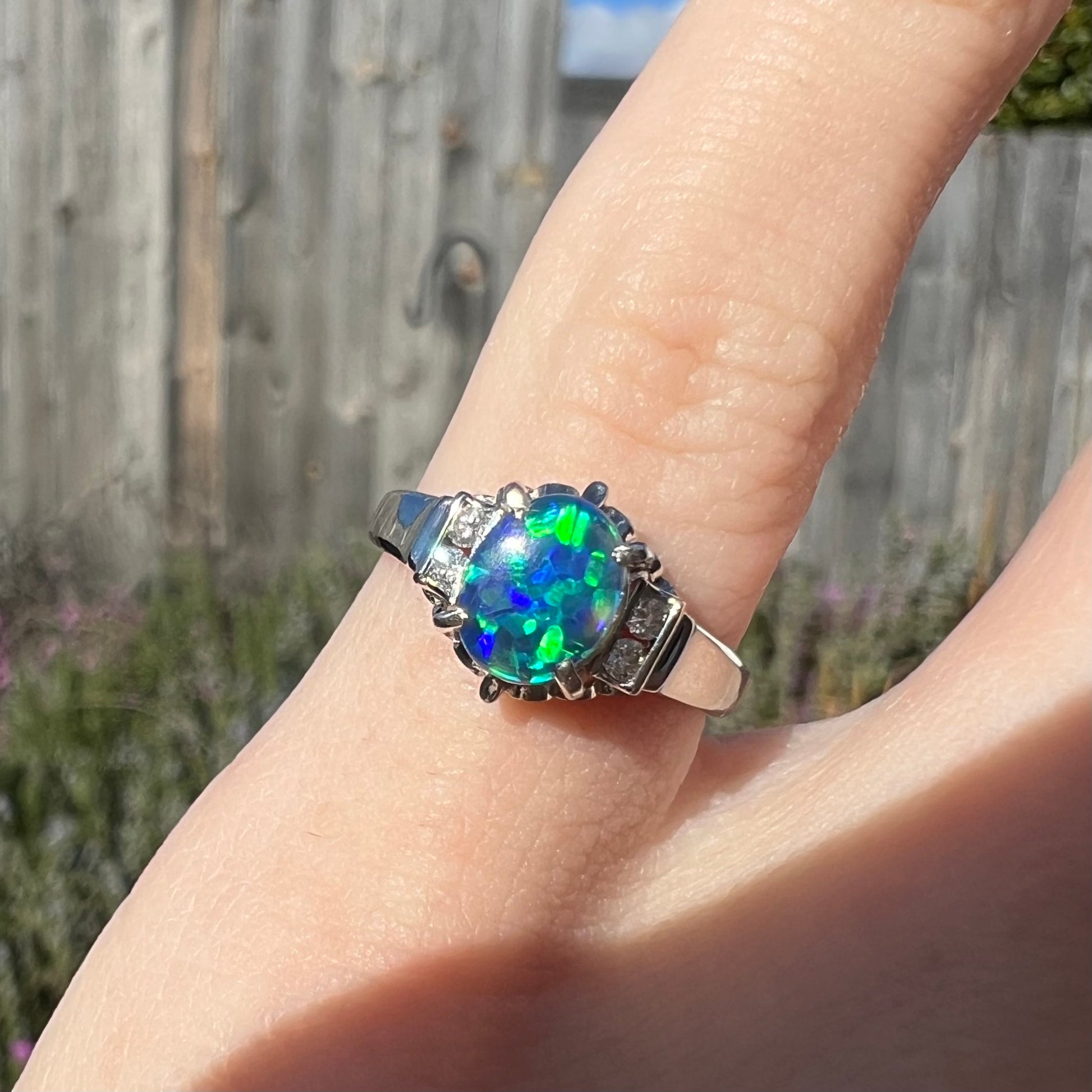 Glowing colors of green and blue play across the surface of a Lightning Ridge black opal, set in a platinum and diamond-accented ring.