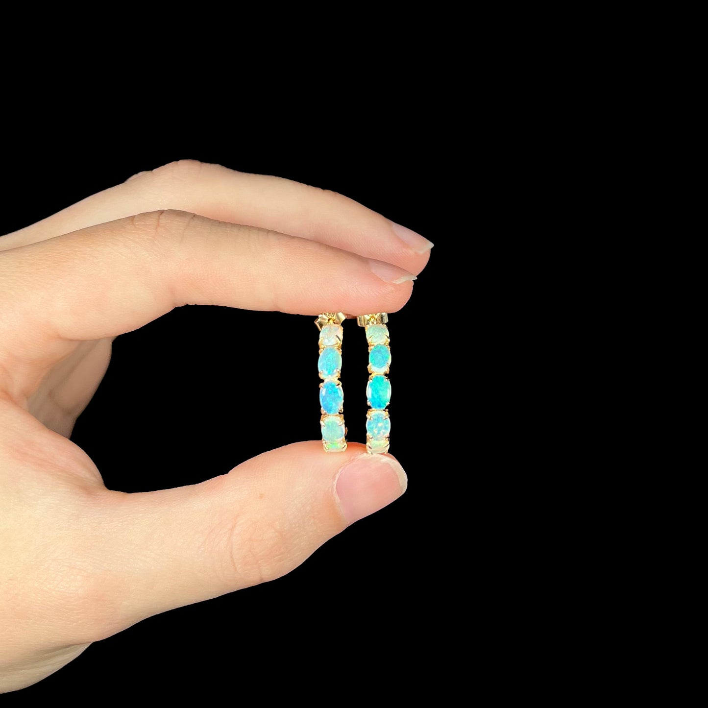 Crystal opal hoop earrings held in hand against black background with green and blue play.