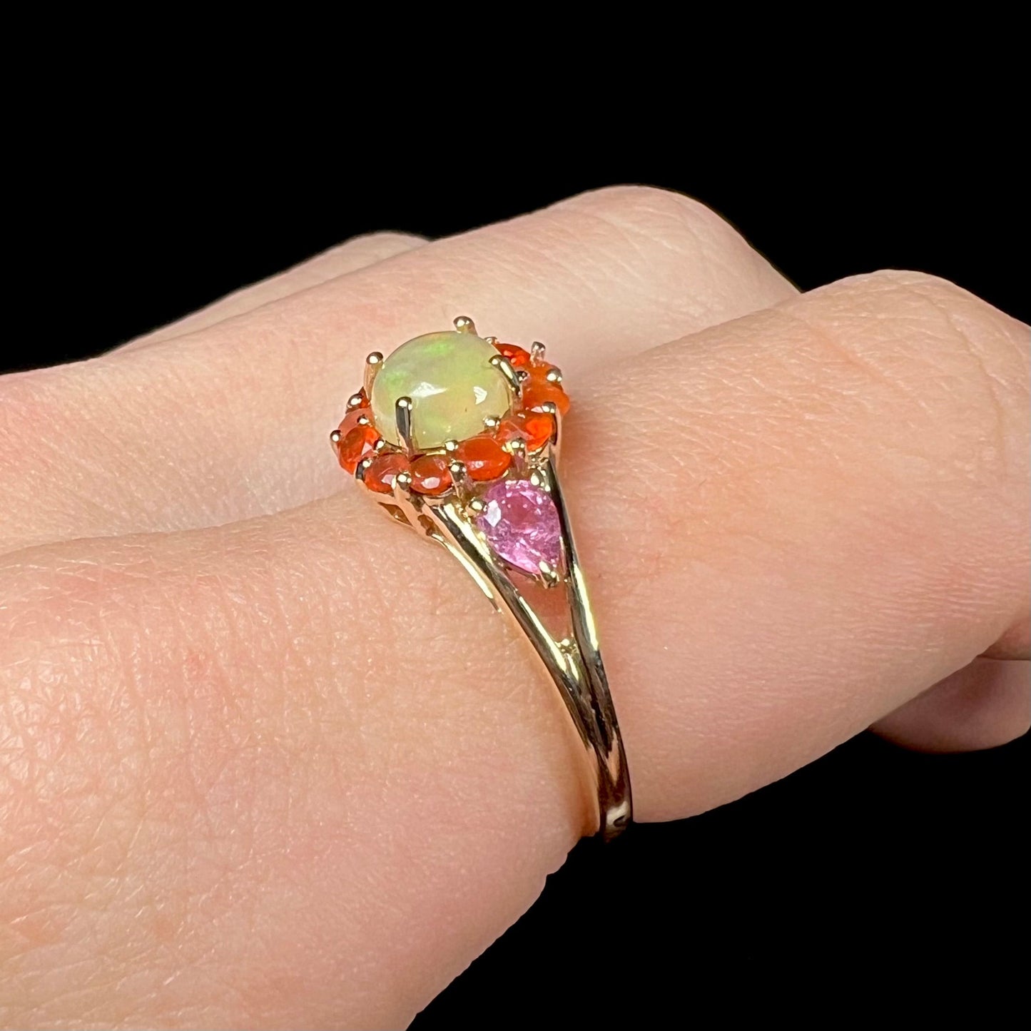 A yellow gold ring mounted with a round Ethiopian opal in a halo of faceted Mexican fire opals. Two pear shaped pink tourmalines accent the sides of the ring.
