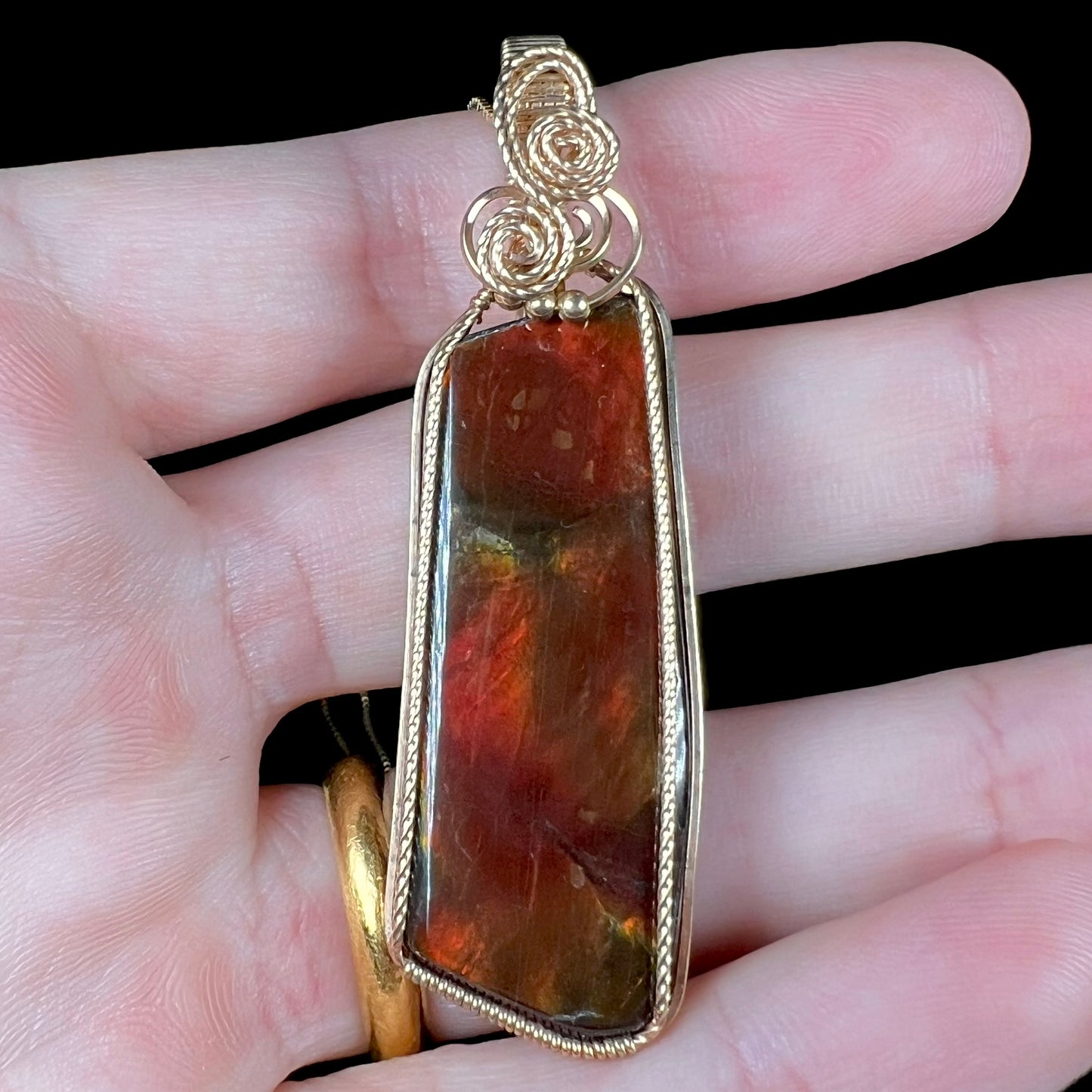 Close-up front view of a gold filled ammolite pendant with red iridescence.