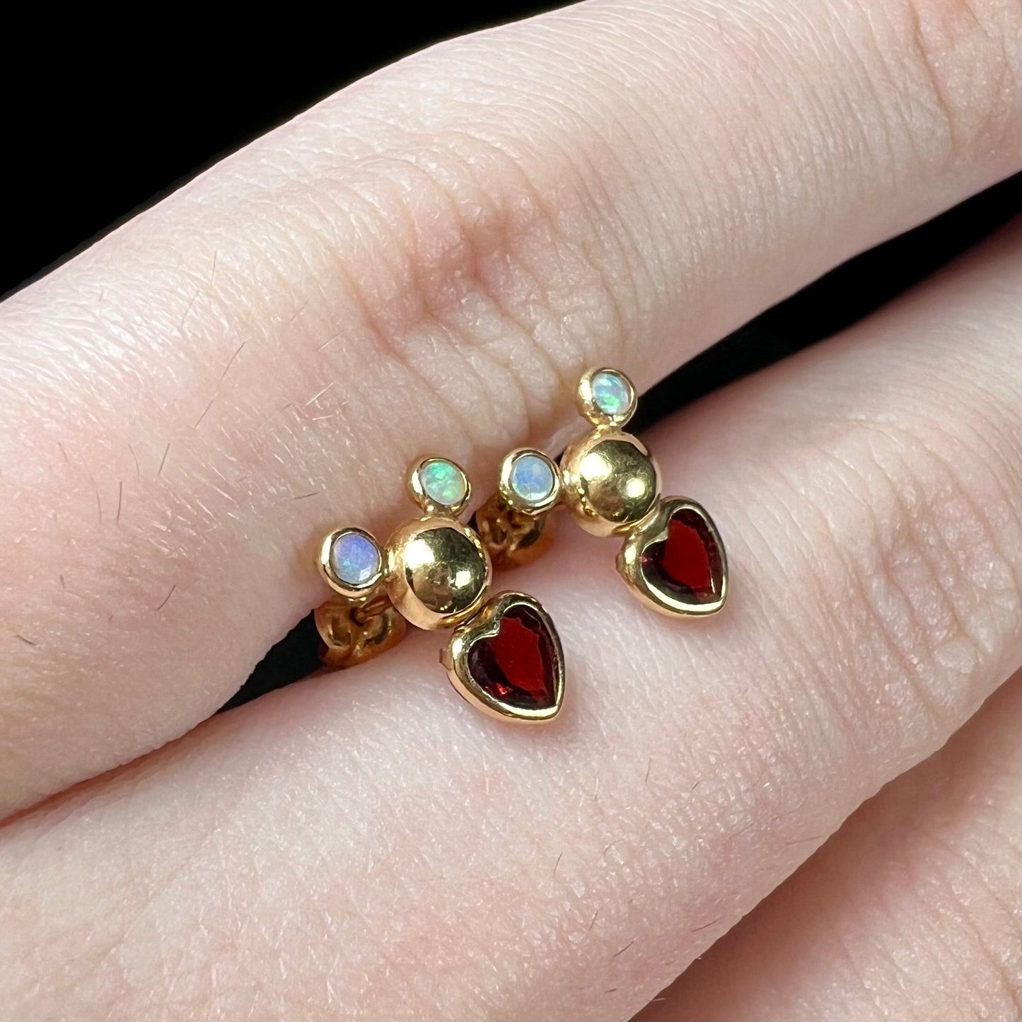 A pair of 18 karat yellow gold stud earrings set with two round fire opals and heart shaped garnets.