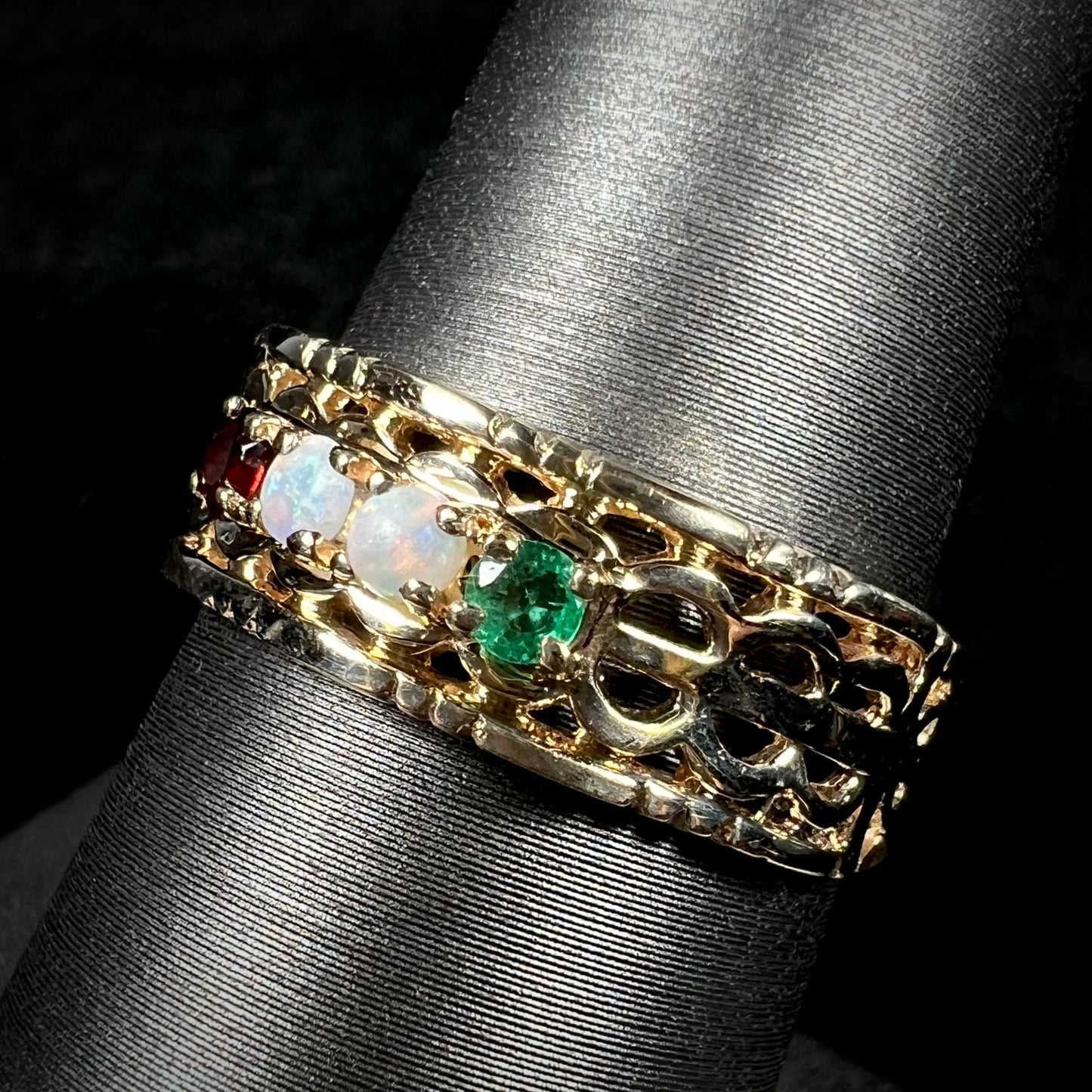 Angled view of a gold woven-style mother's ring set with two opals, an emerald, and a garnet.